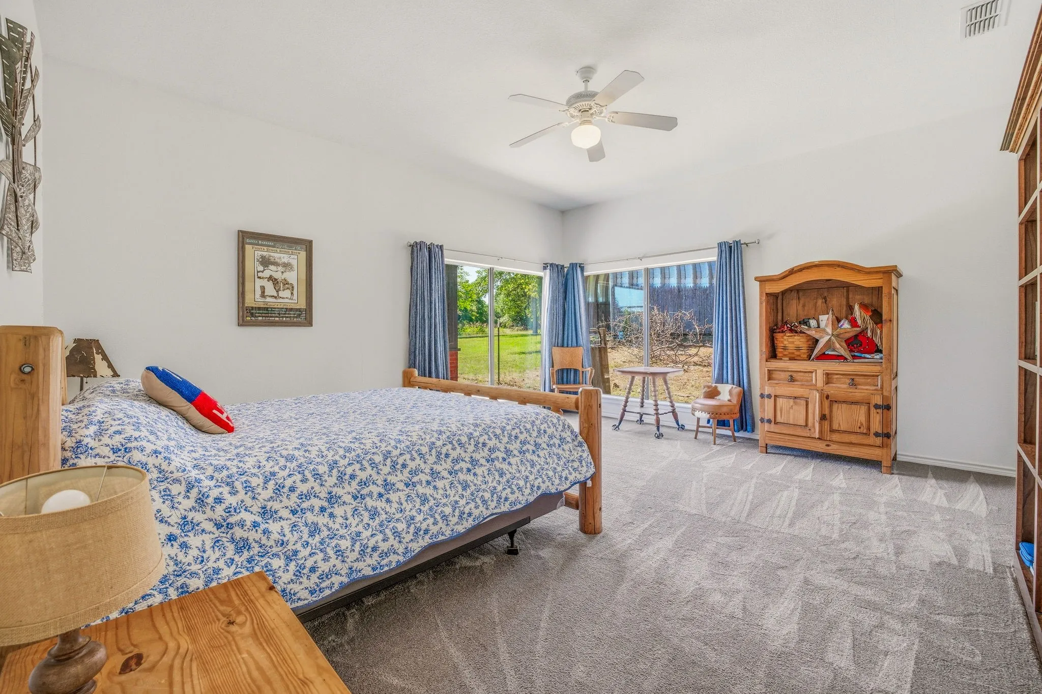 Spacious room with light gray carpeting, ceiling fan with light, and bay windows featuring outdoor views