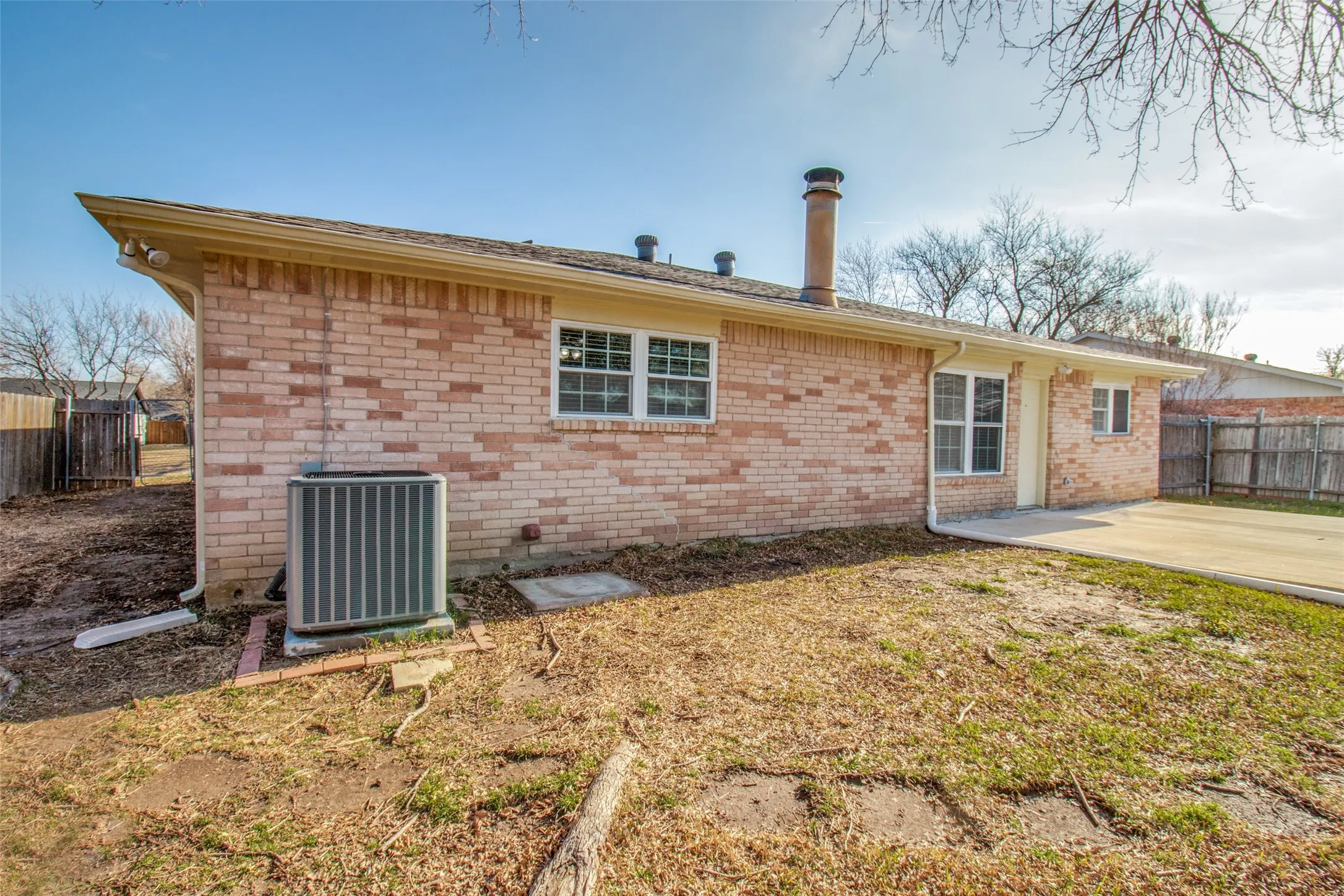 Brick exterior featuring a concrete patio, multiple windows, a chimney, and an HVAC unit