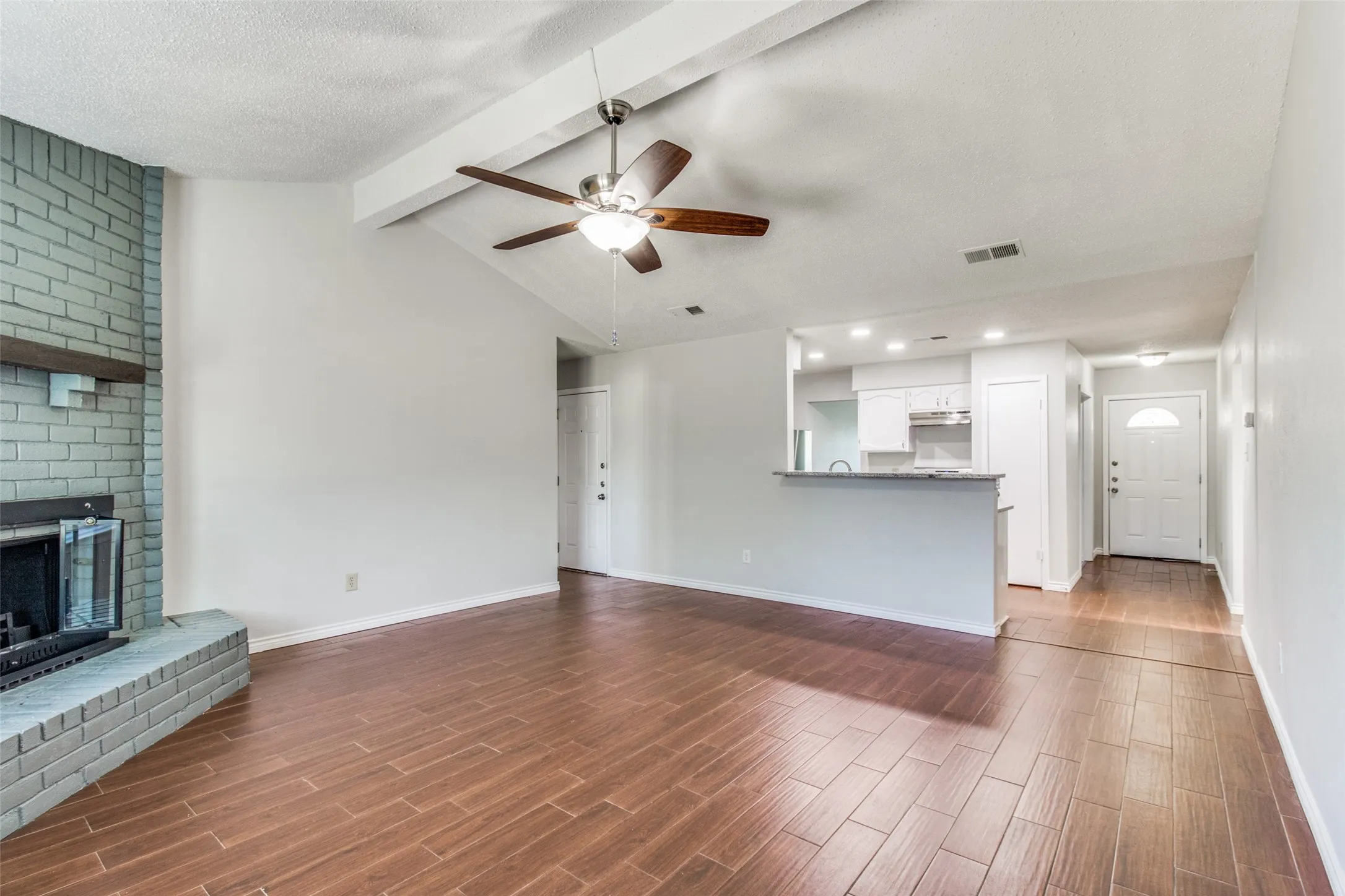 Spacious living area featuring wood-finish flooring, a vaulted ceiling with exposed beam, and a ceiling fan
