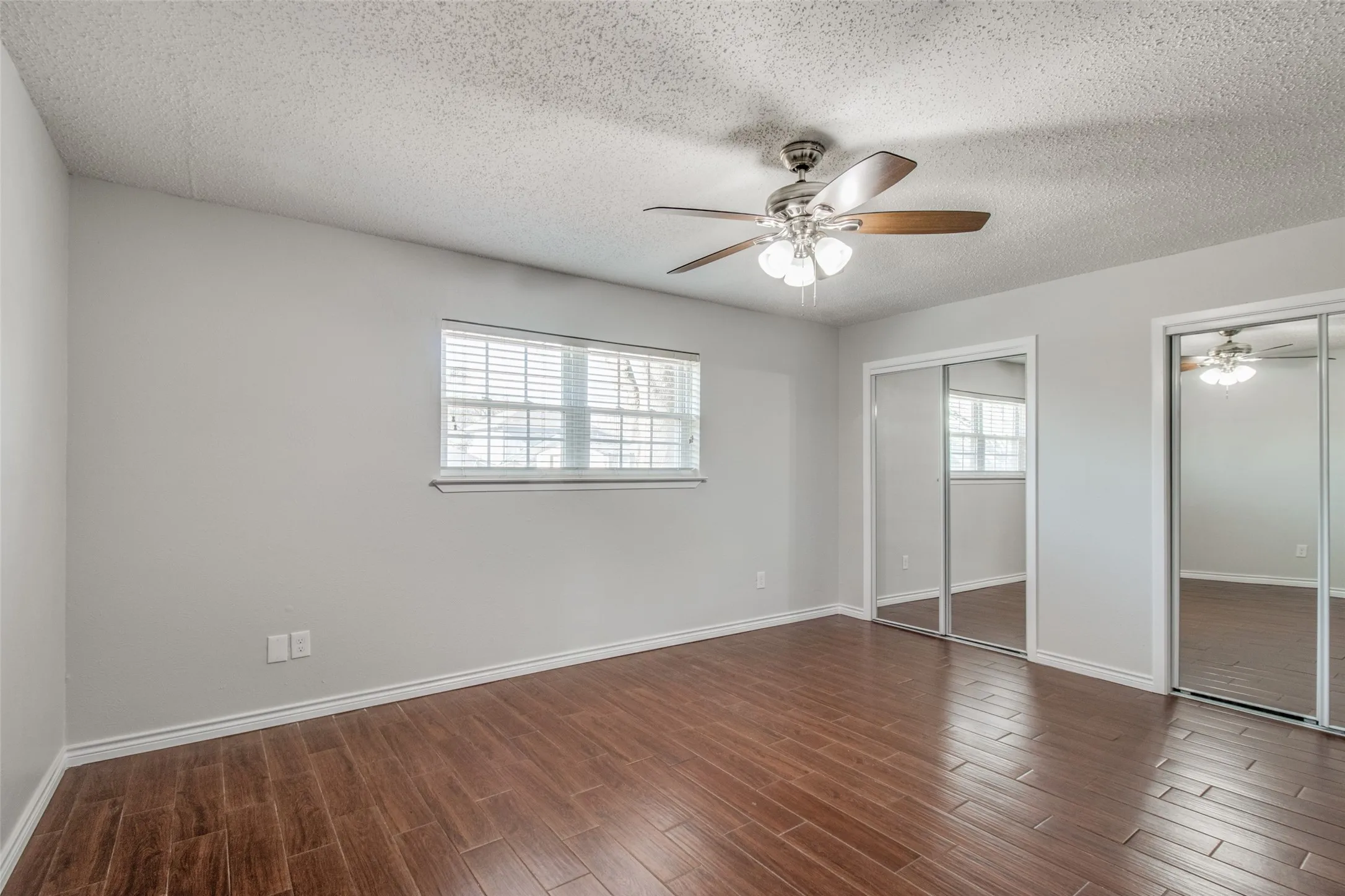 Bedroom featuring wood-finish flooring, light gray walls, white baseboards, and a window with blinds