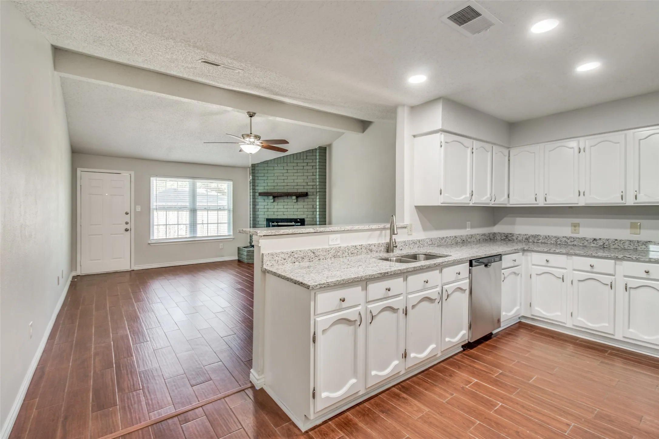 Kitchen featuring white cabinetry, light-toned countertops, a double basin sink with a chrome faucet, and stainless steel dishwasher