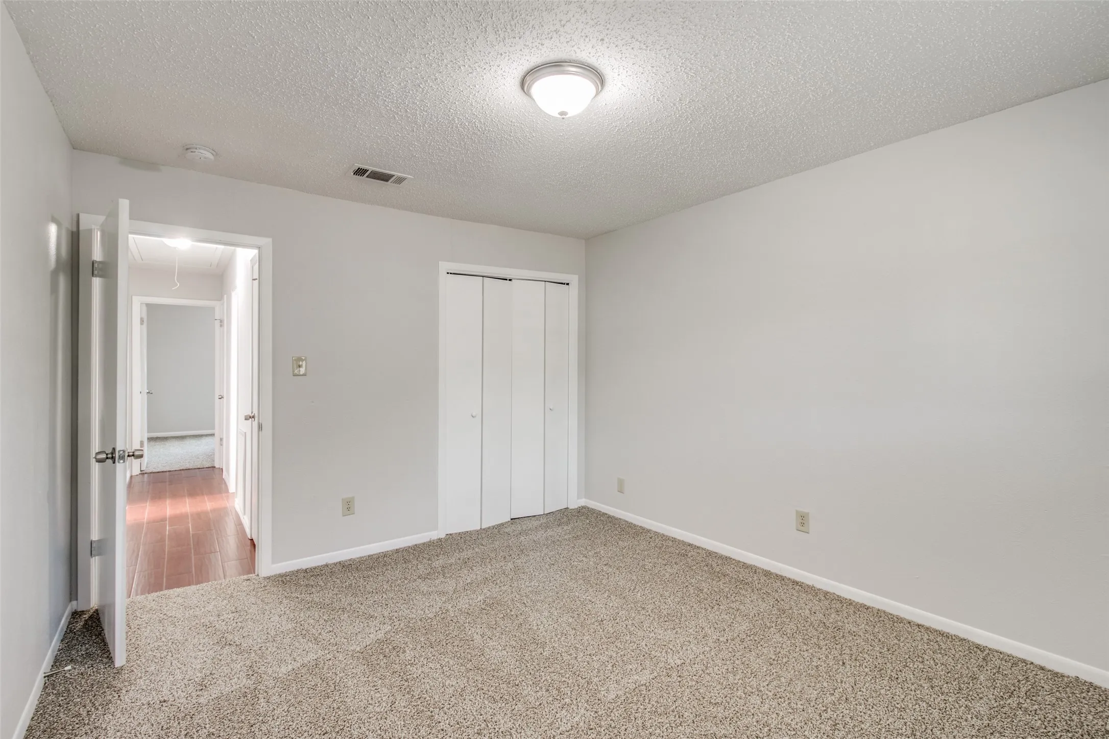 Carpeted room with light gray walls, a flush-mount ceiling light fixture, and bifold closet doors