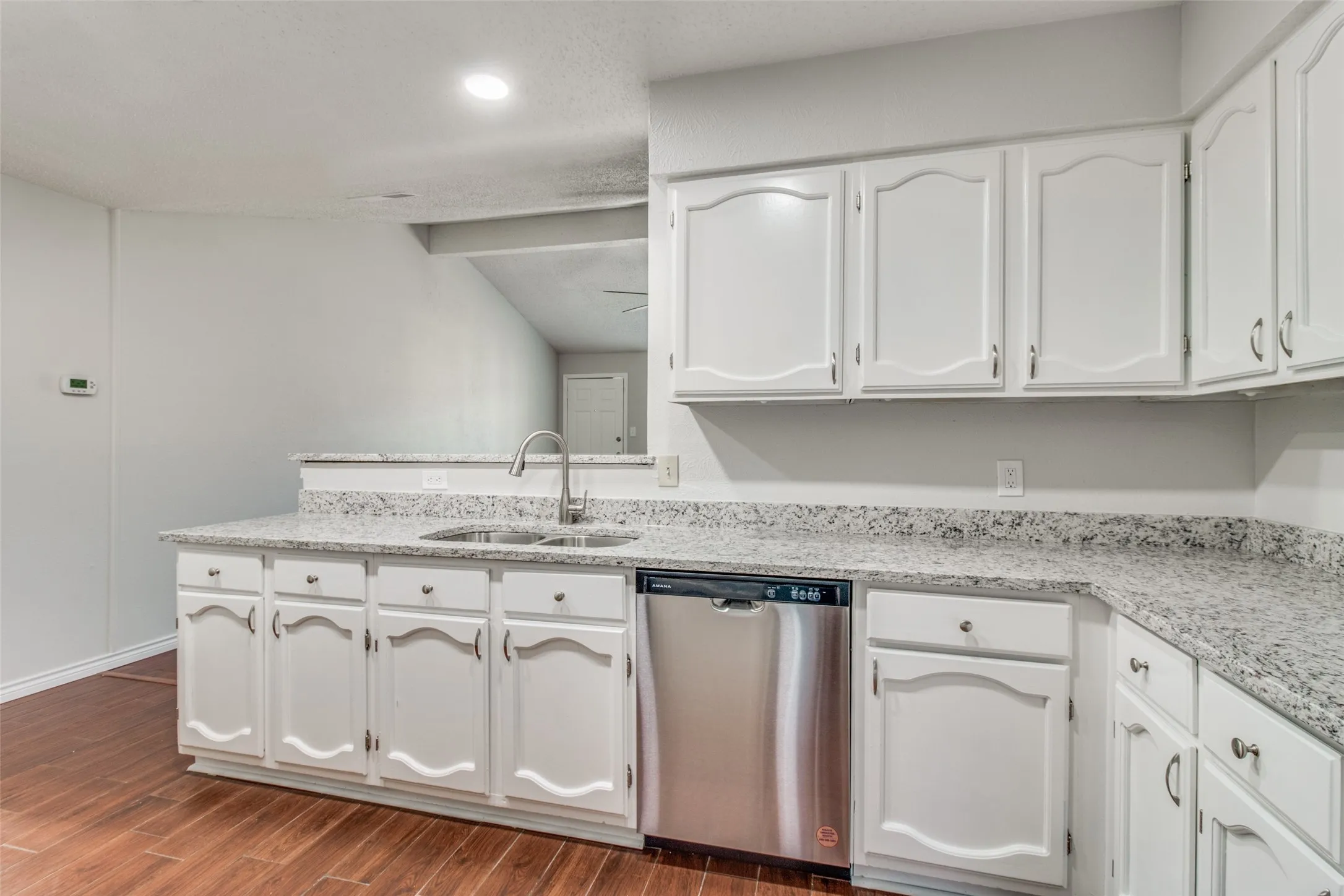 Kitchen with white cabinetry, speckled countertops, and wood-finish flooring