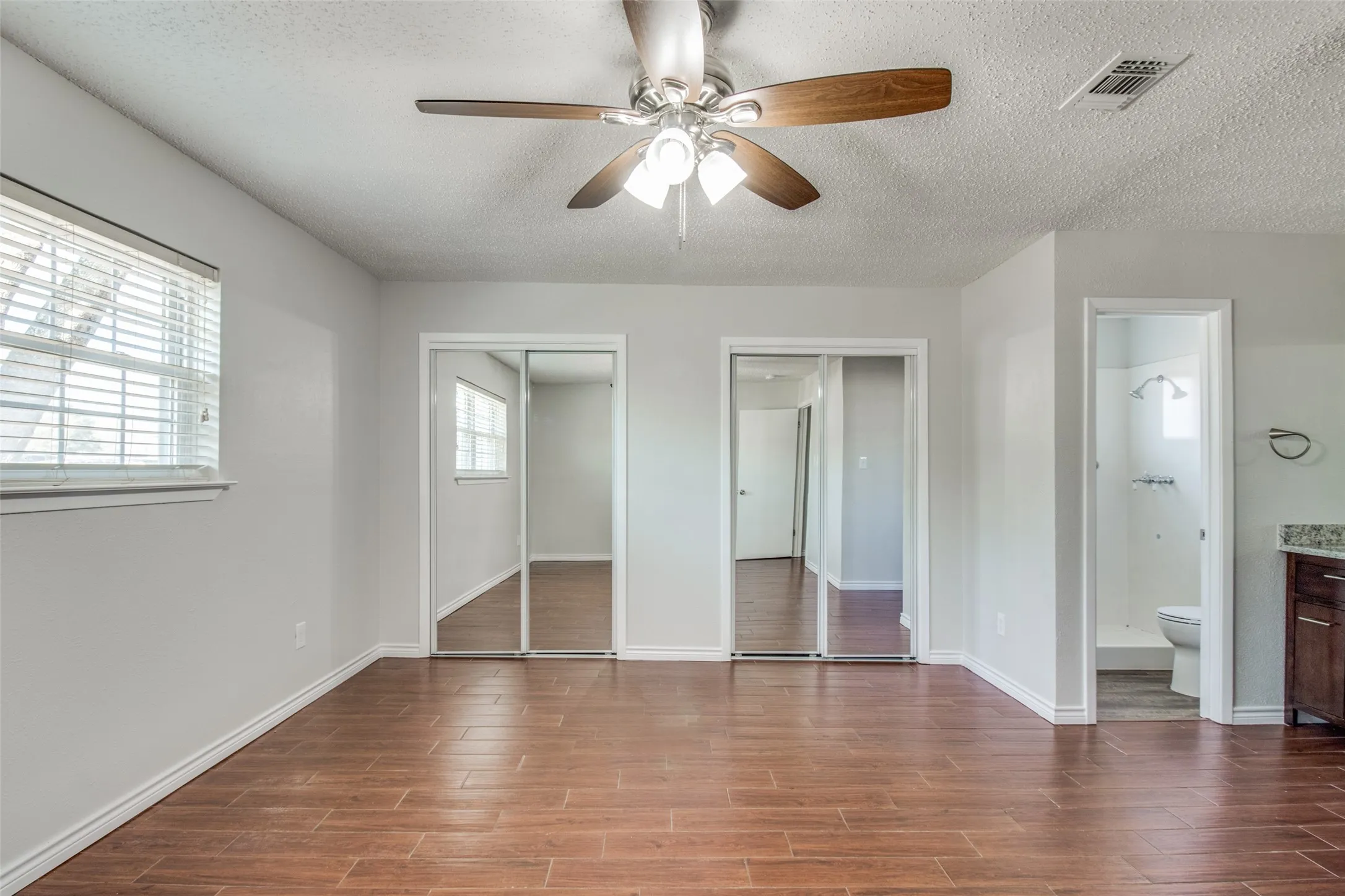 Spacious room featuring wood-finish flooring, a ceiling fan with integrated lighting, and a window with blinds
