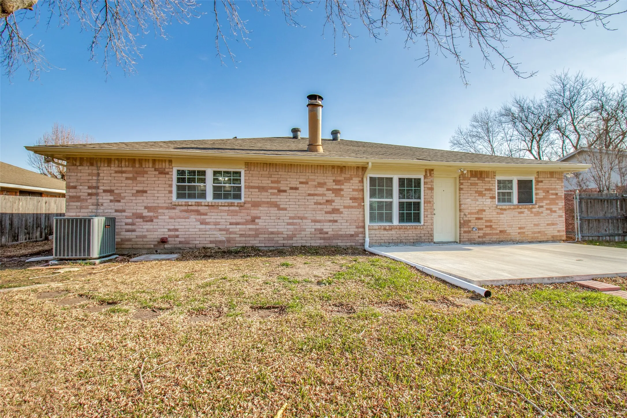 Brick exterior featuring a concrete patio, multiple windows, and a rear entry door
