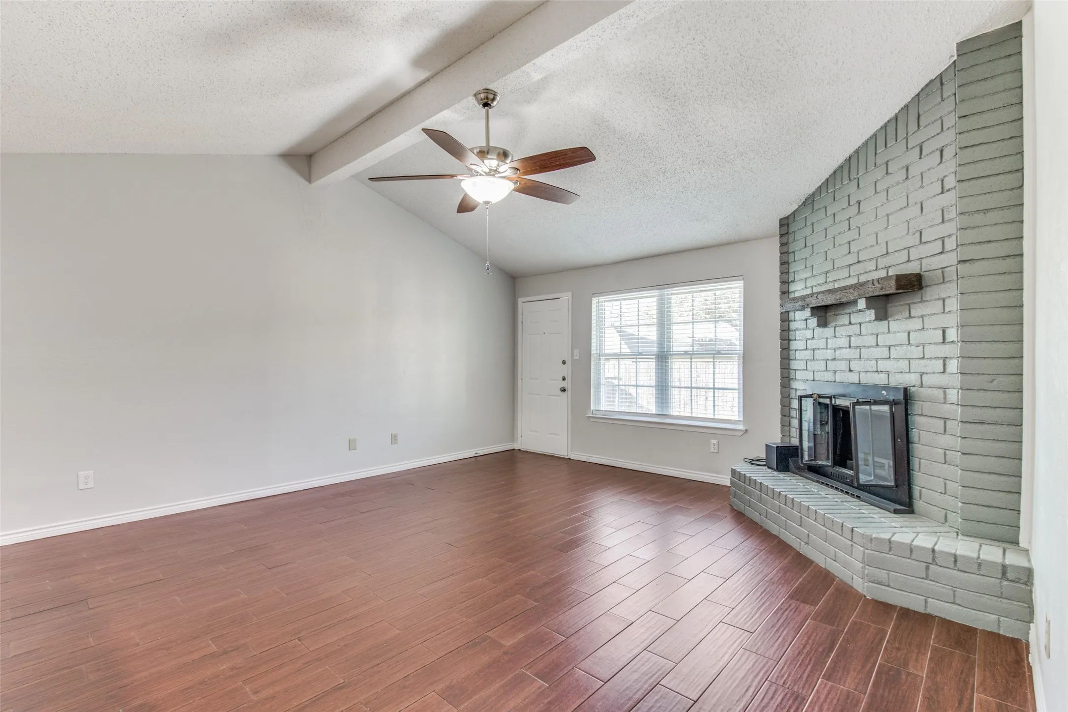 Spacious living area featuring a brick fireplace with wood mantel, vaulted ceiling, wood-finish flooring, and a ceiling fan