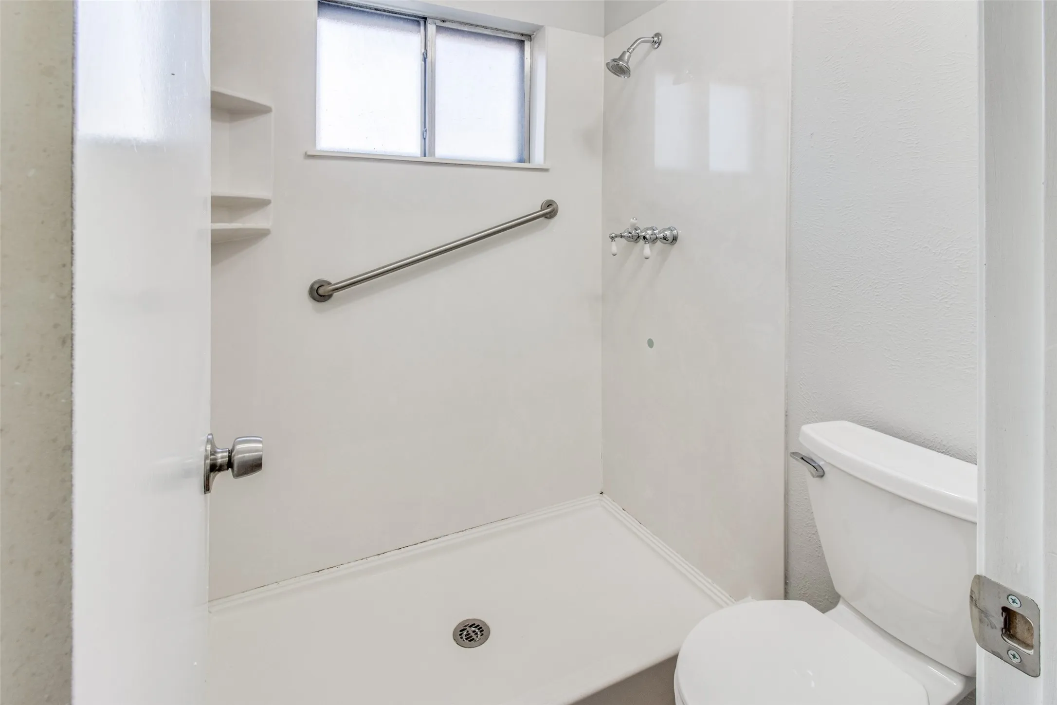 Walk-in shower with a chrome showerhead, grab bar, and built-in shelving