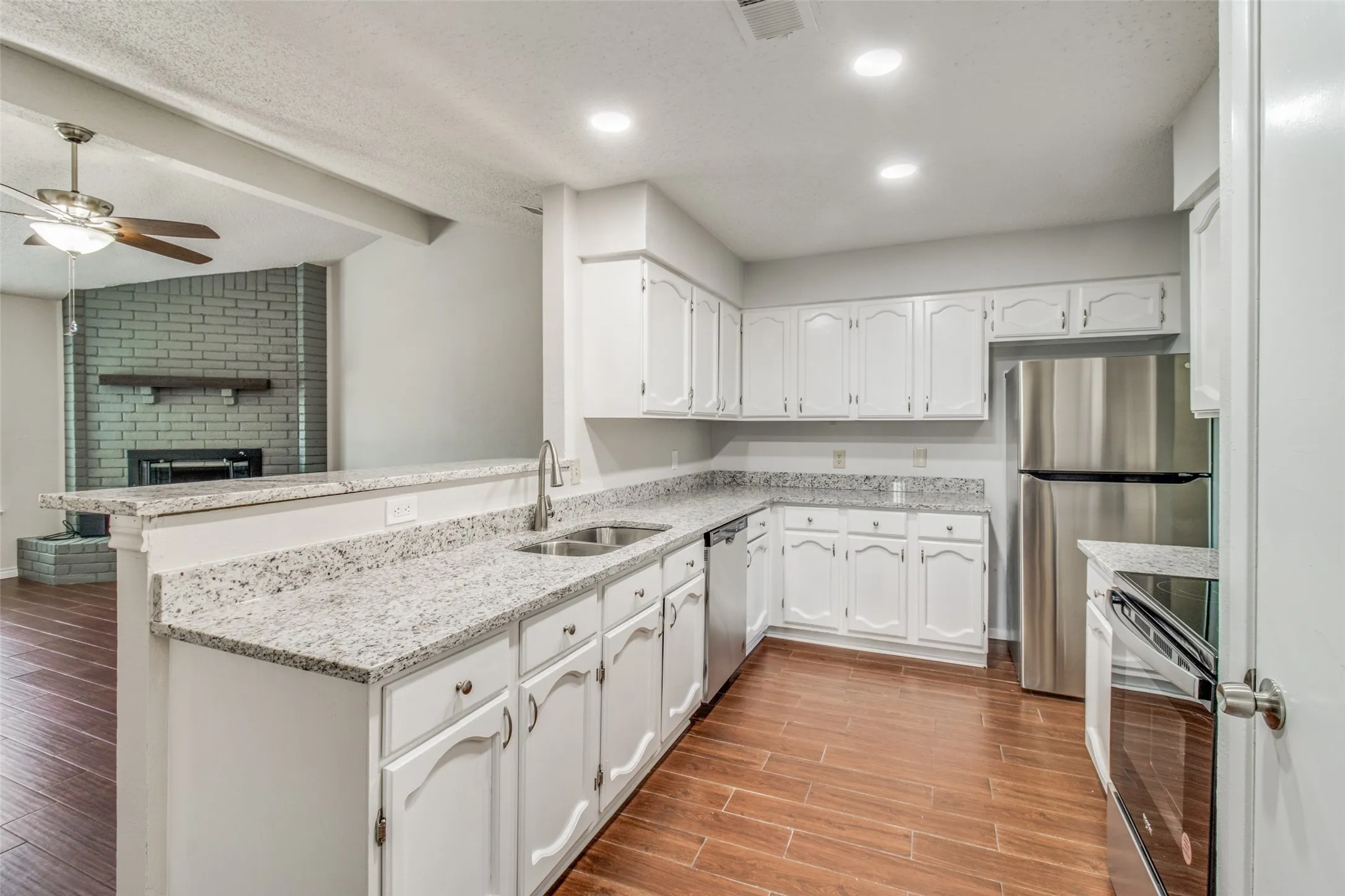 Kitchen featuring white cabinetry, light-toned countertops, stainless steel appliances, and wood-finish flooring