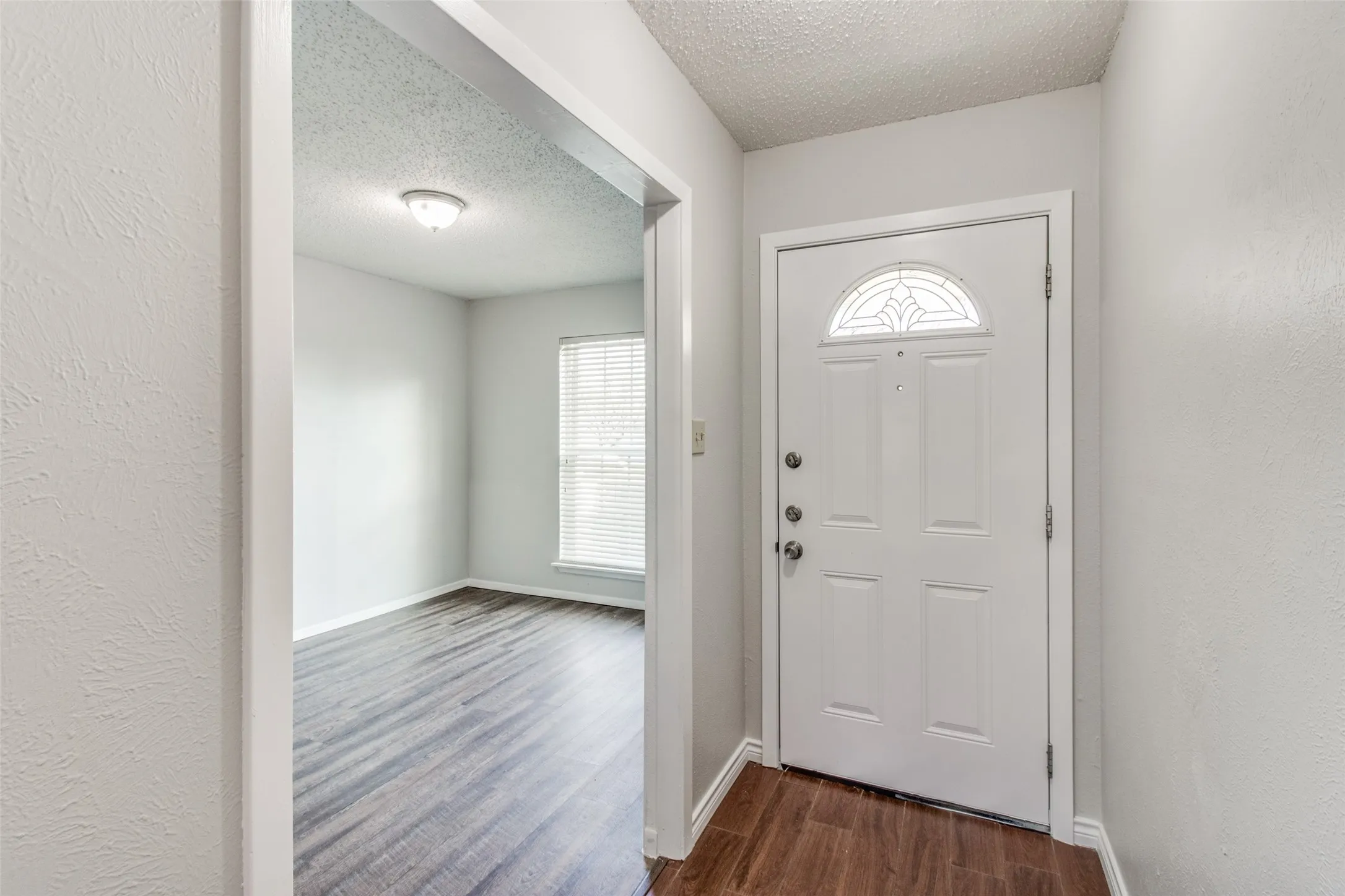 Entryway featuring a white paneled door with an arched decorative glass insert and dark wood-finish flooring