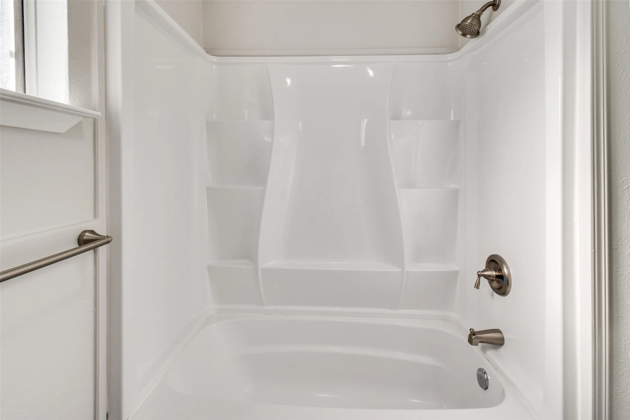 Bathtub and shower combination featuring a white composite surround with integrated shelving and brushed nickel fixtures
