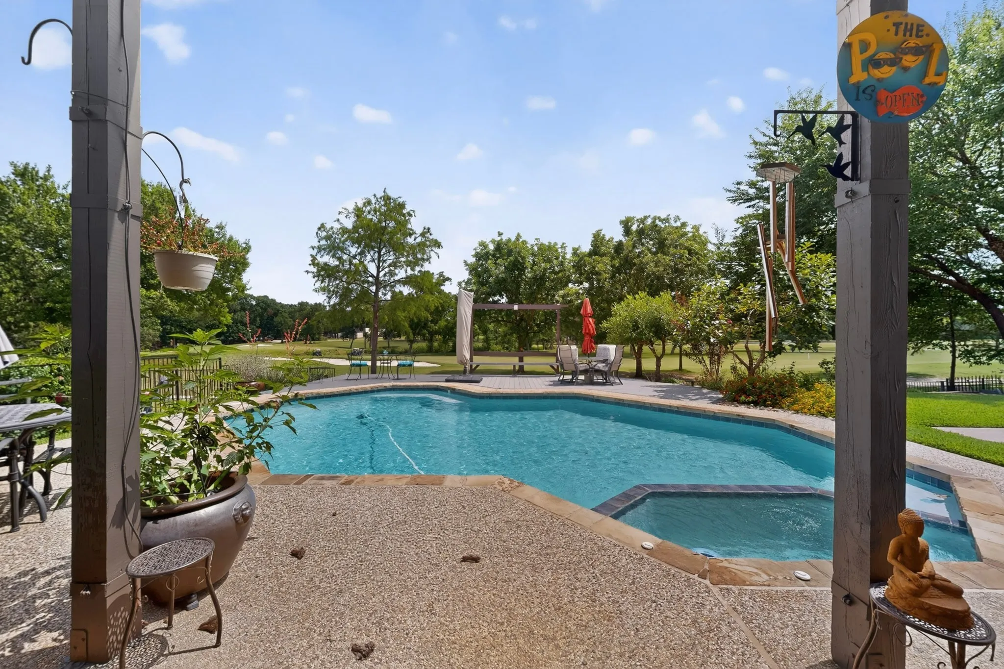 Outdoor living area featuring an in-ground swimming pool with an integrated spa, expansive exposed aggregate patio, and mature trees