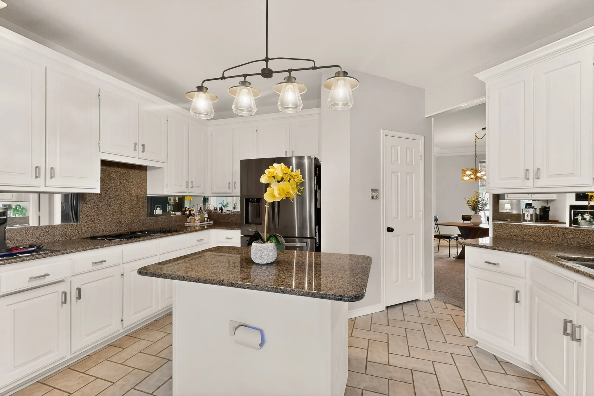 Kitchen featuring white cabinetry, granite countertops, a central island, stainless steel refrigerator, and herringbone tile flooring