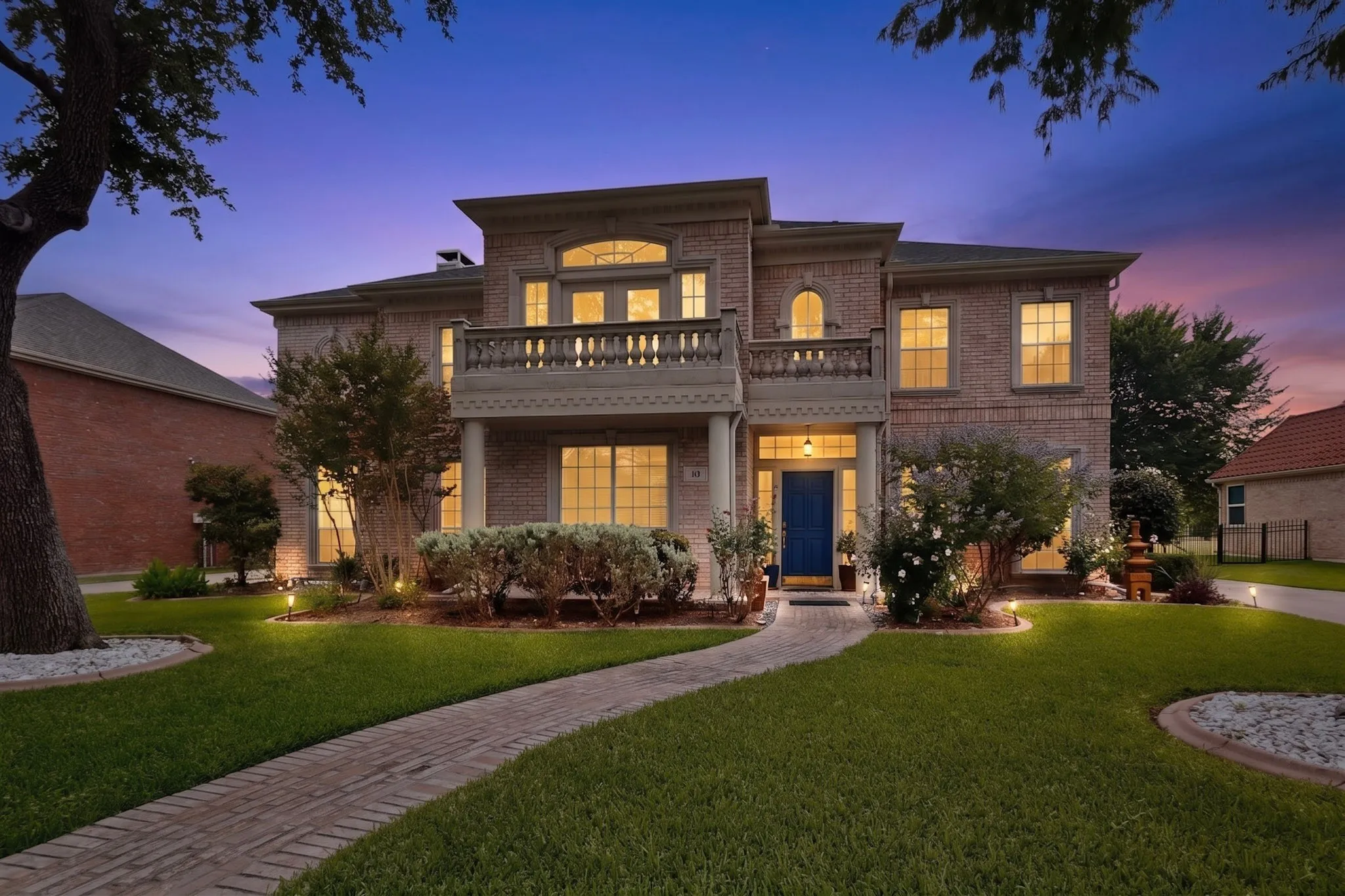 Brick facade residence featuring a second-story balcony with balustrade, arched window accents, and a contrasting blue front door