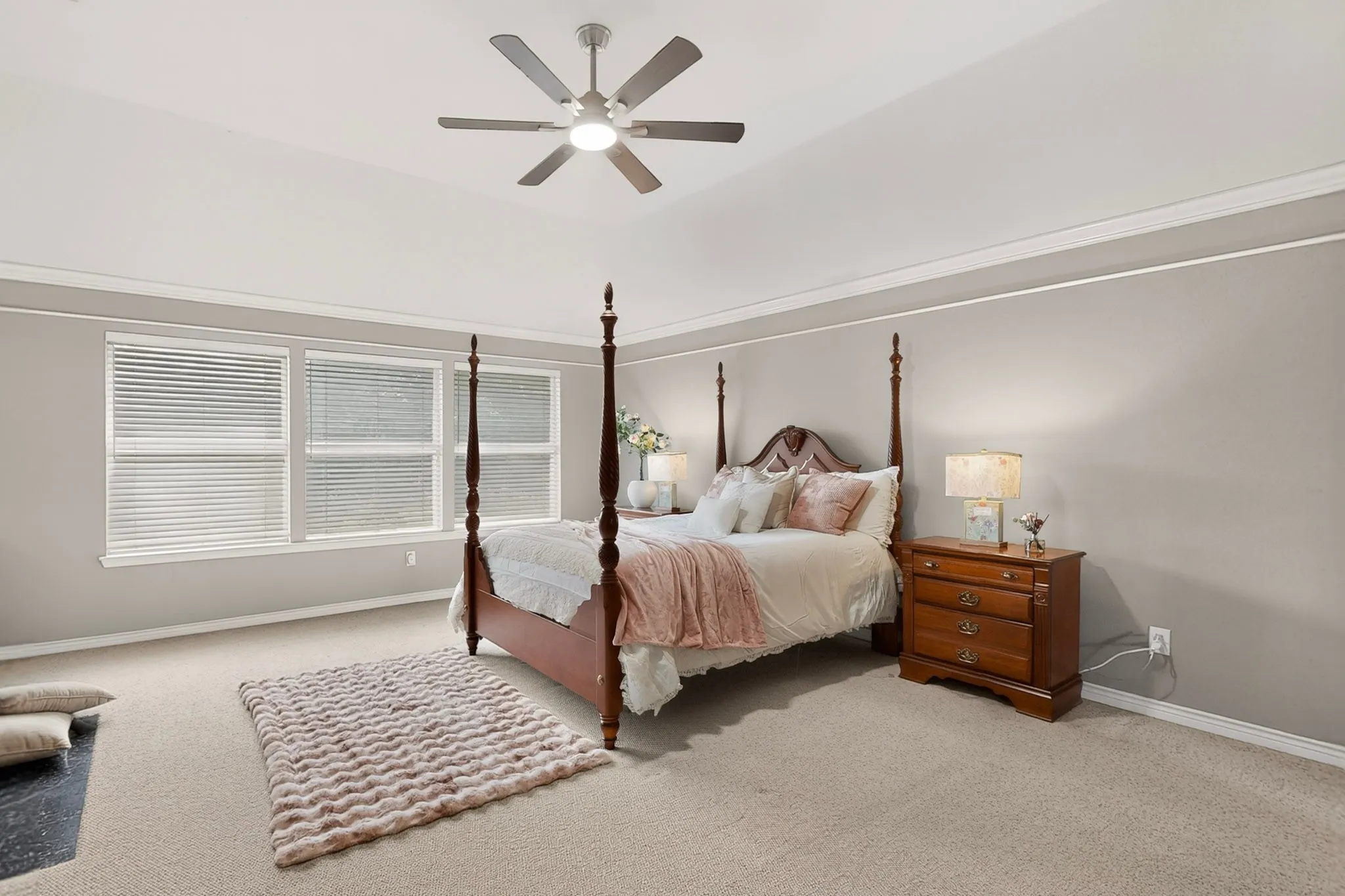 Carpeted room featuring a vaulted ceiling with a ceiling fan, crown molding, and a row of three windows with blinds