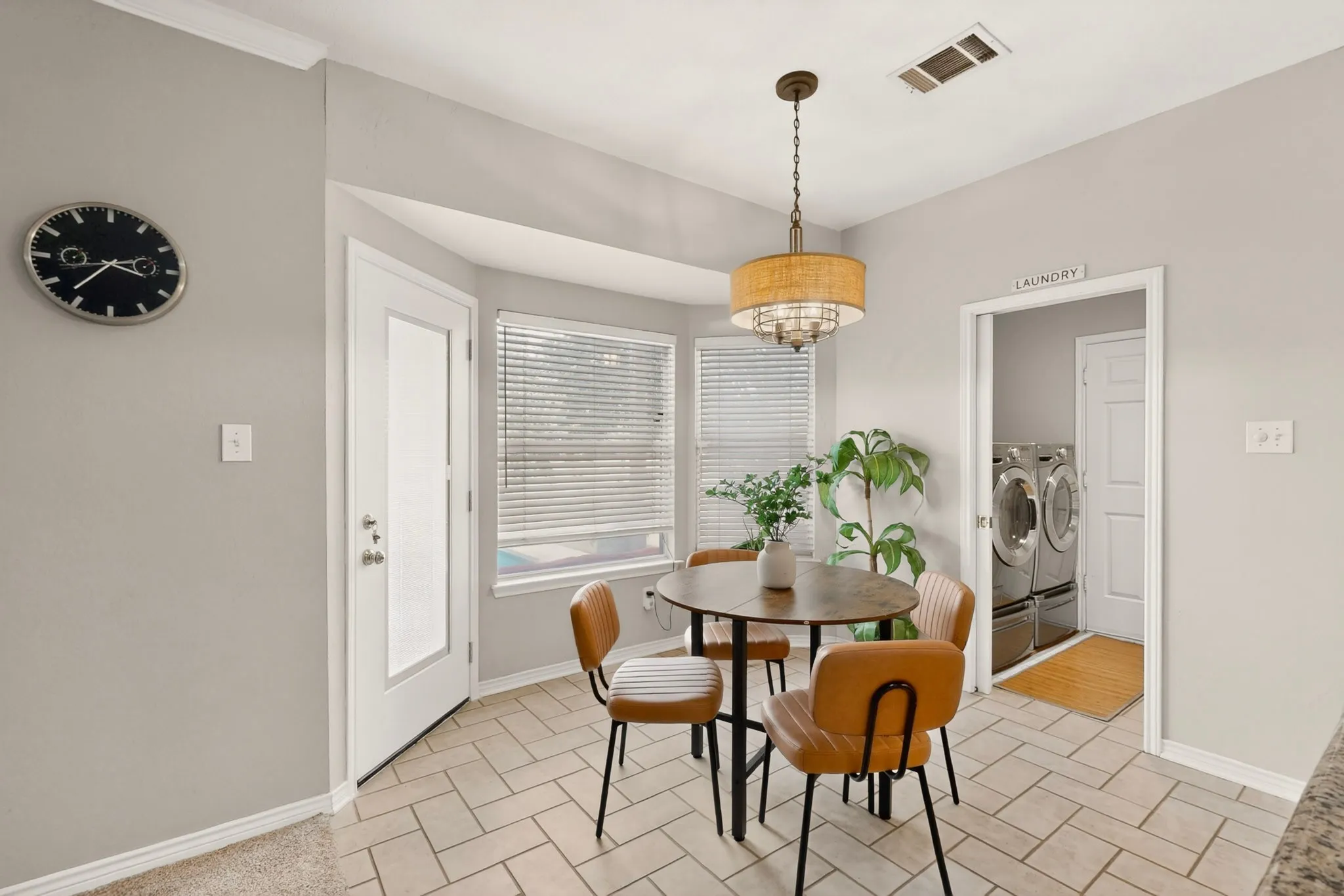 Tiled flooring throughout this bright breakfast nook, featuring a bay window, decorative chandelier, and exterior door with frosted glass panel