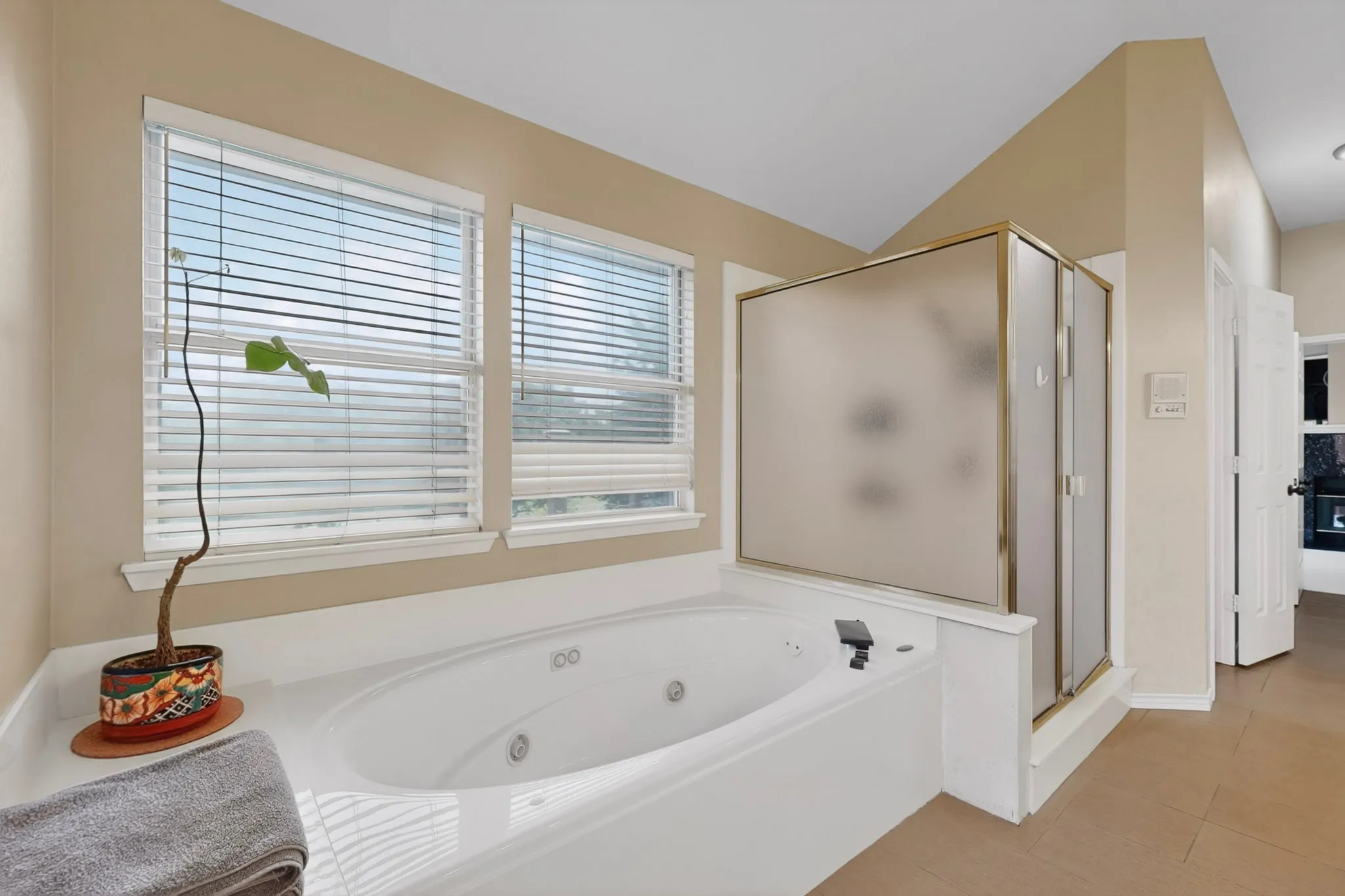 Built-in soaking tub with white surround, two horizontal windows, and a glass-enclosed shower with a gold-tone frame