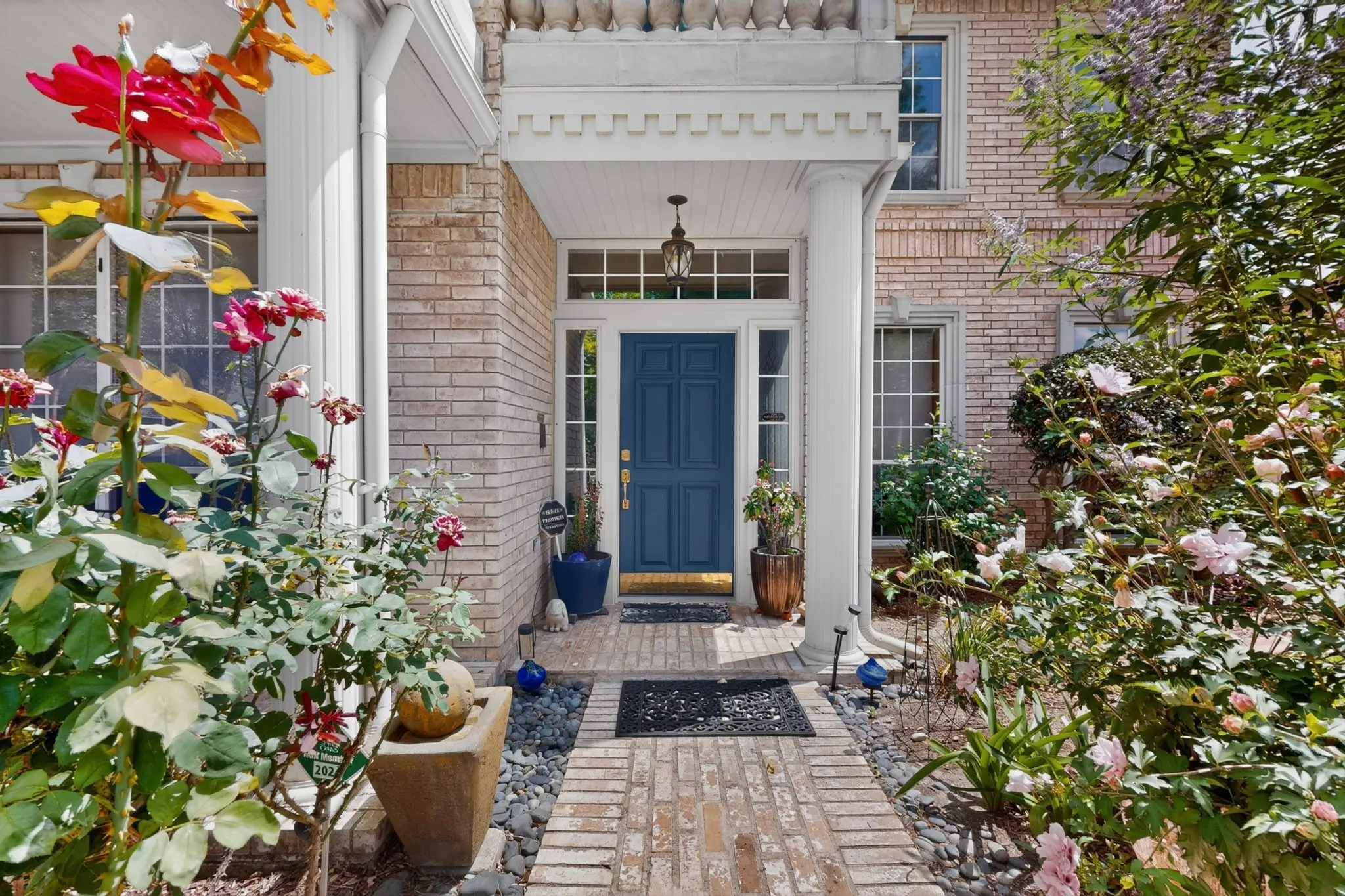 Brick facade entrance featuring a covered porch with white columns, a blue paneled door, and a transom window