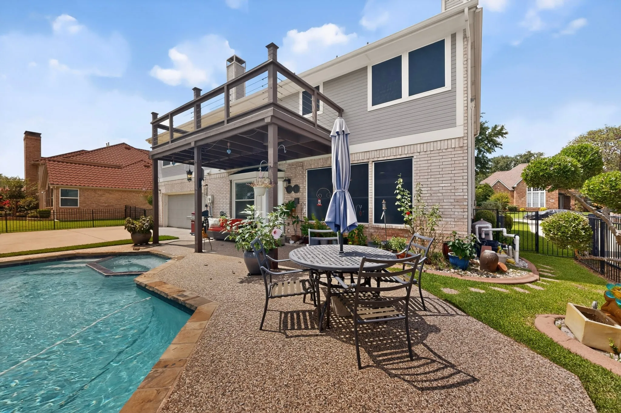 Expansive backyard featuring a built-in pool with spa, an upper deck with cable railing, a covered patio, and a gravel-finish patio