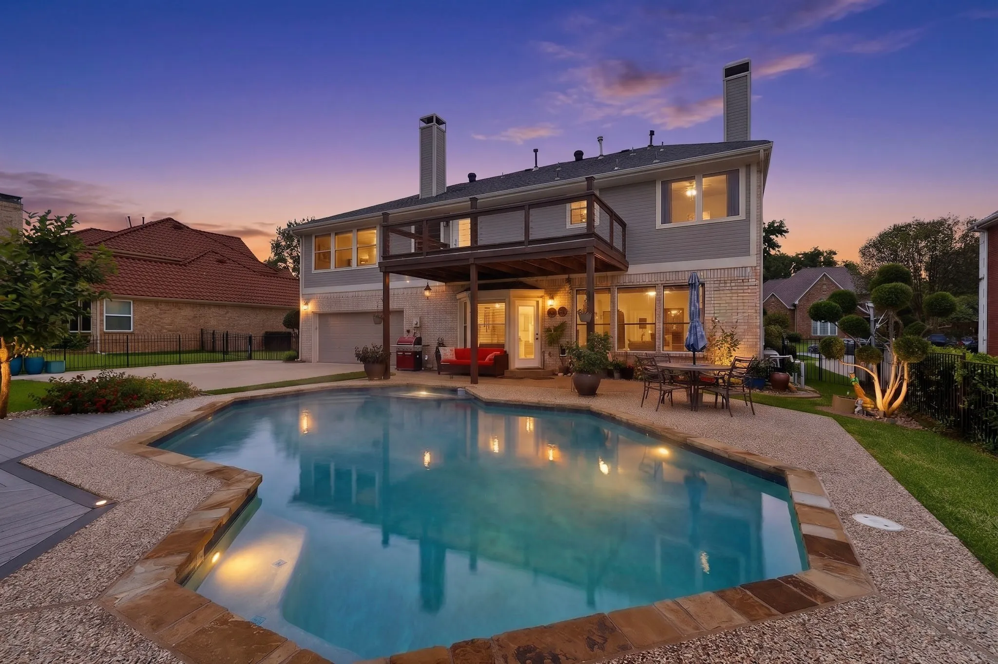 Rear exterior featuring a freeform swimming pool with stone coping, an upper-level deck, a lower-level patio, and a two-story residence with brick and siding finishes