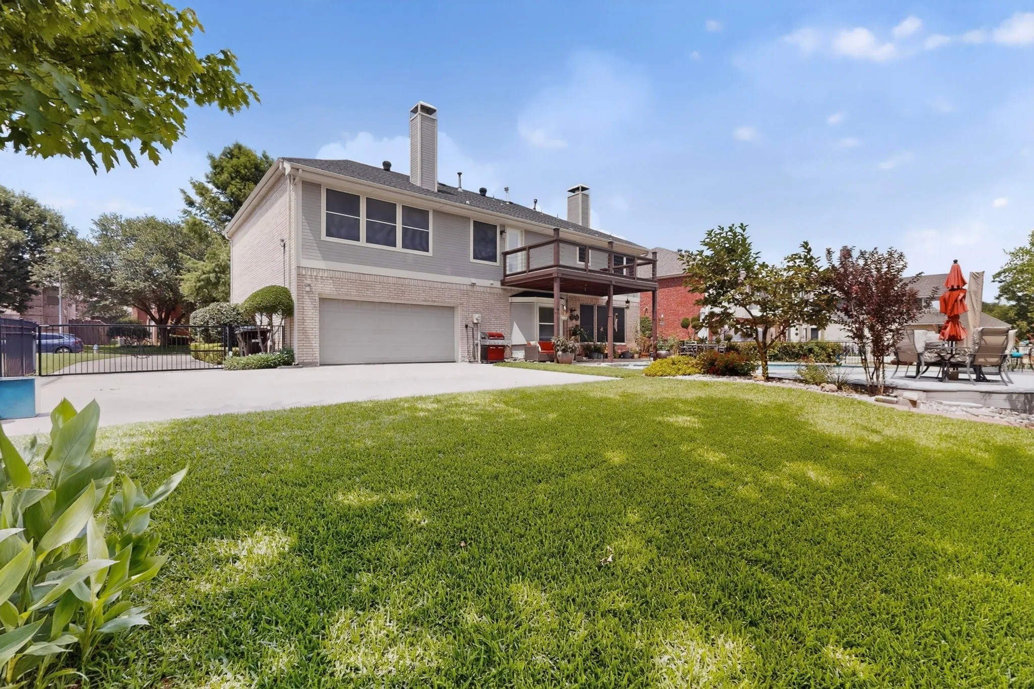 Spacious backyard featuring a large green lawn, mature landscaping, and an expansive pool deck