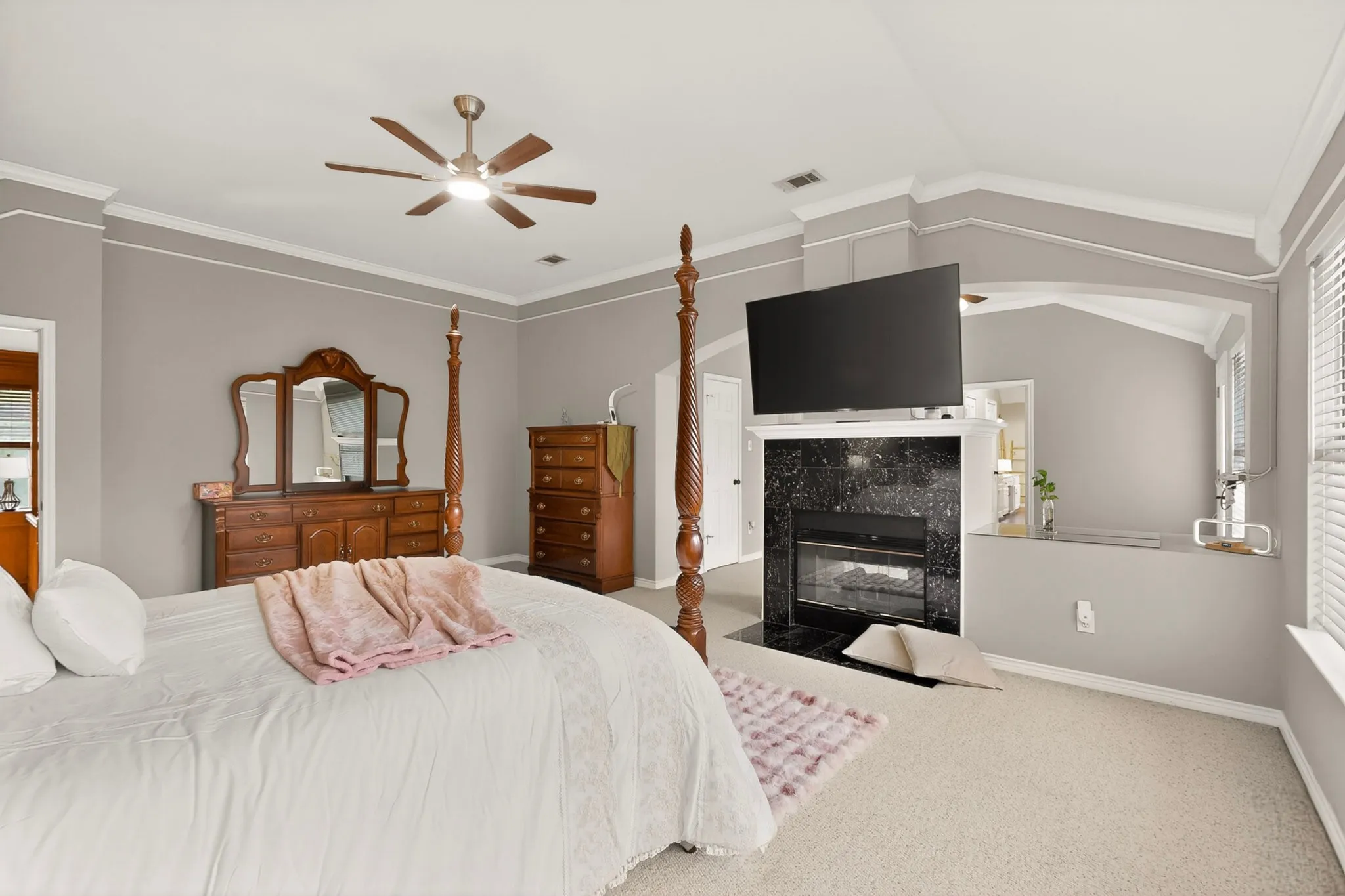 Carpeted bedroom featuring a black stone fireplace surround, high vaulted ceilings, crown molding, and a ceiling fan with integrated lighting