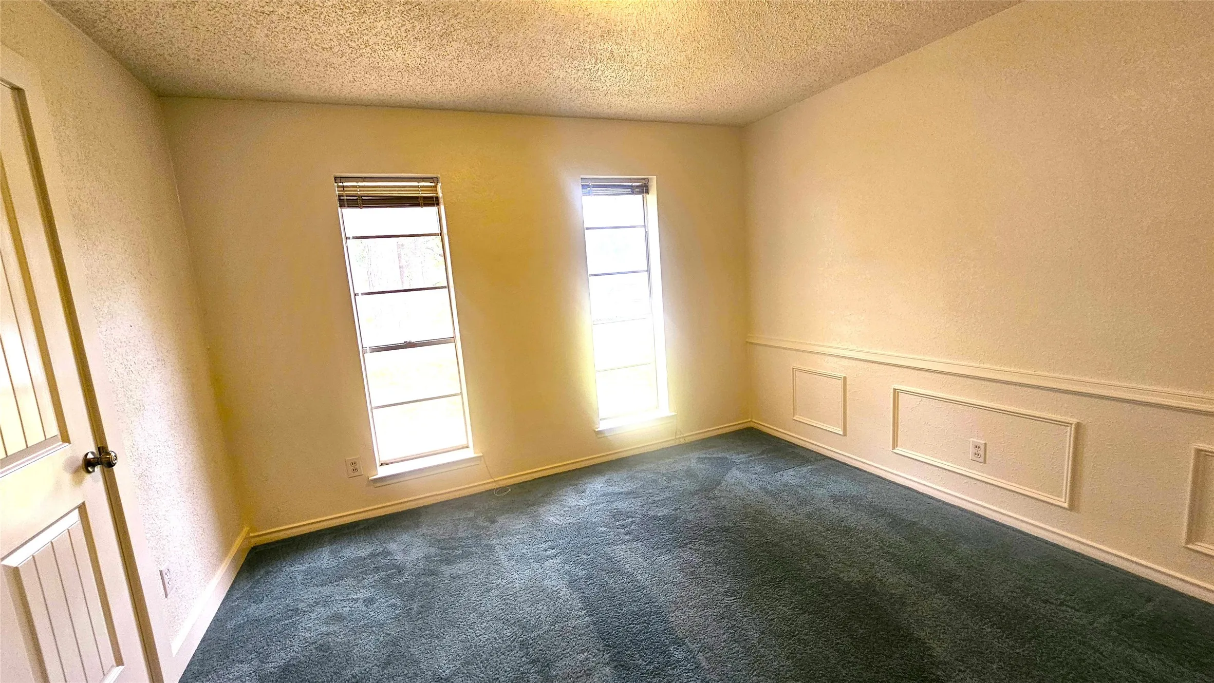 Bedroom 3 with a textured ceiling, blue carpet, and baseboards windows facing front of house.
