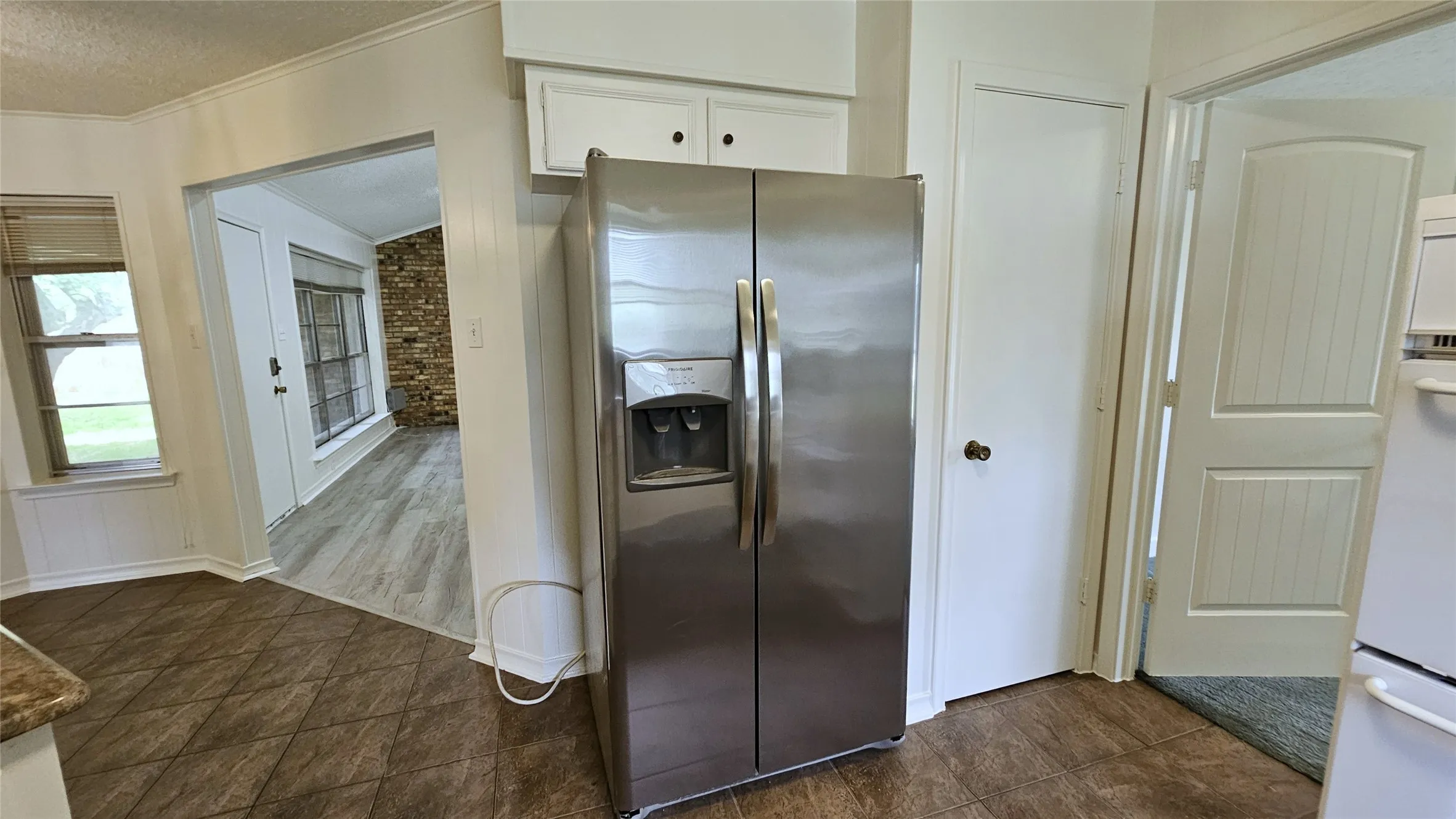 Kitchen with stainless steel refrigerator with ice dispenser, white cabinetry, a textured ceiling, crown molding, and baseboards, pantry and door to Bedroom 3
