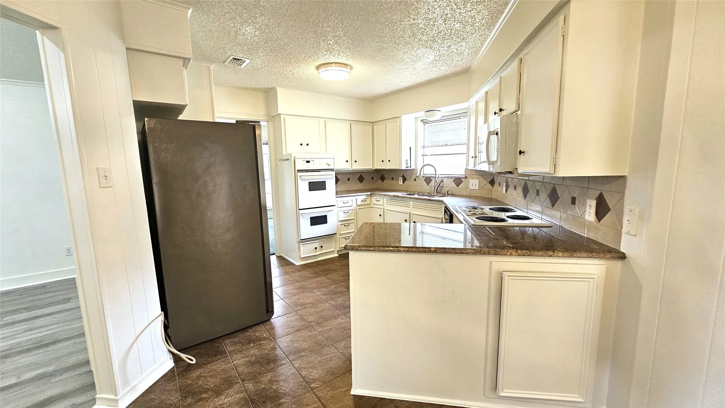 Kitchen with white appliances, a sink, a peninsula, decorative backsplash, and a Stainless steel refrigerator