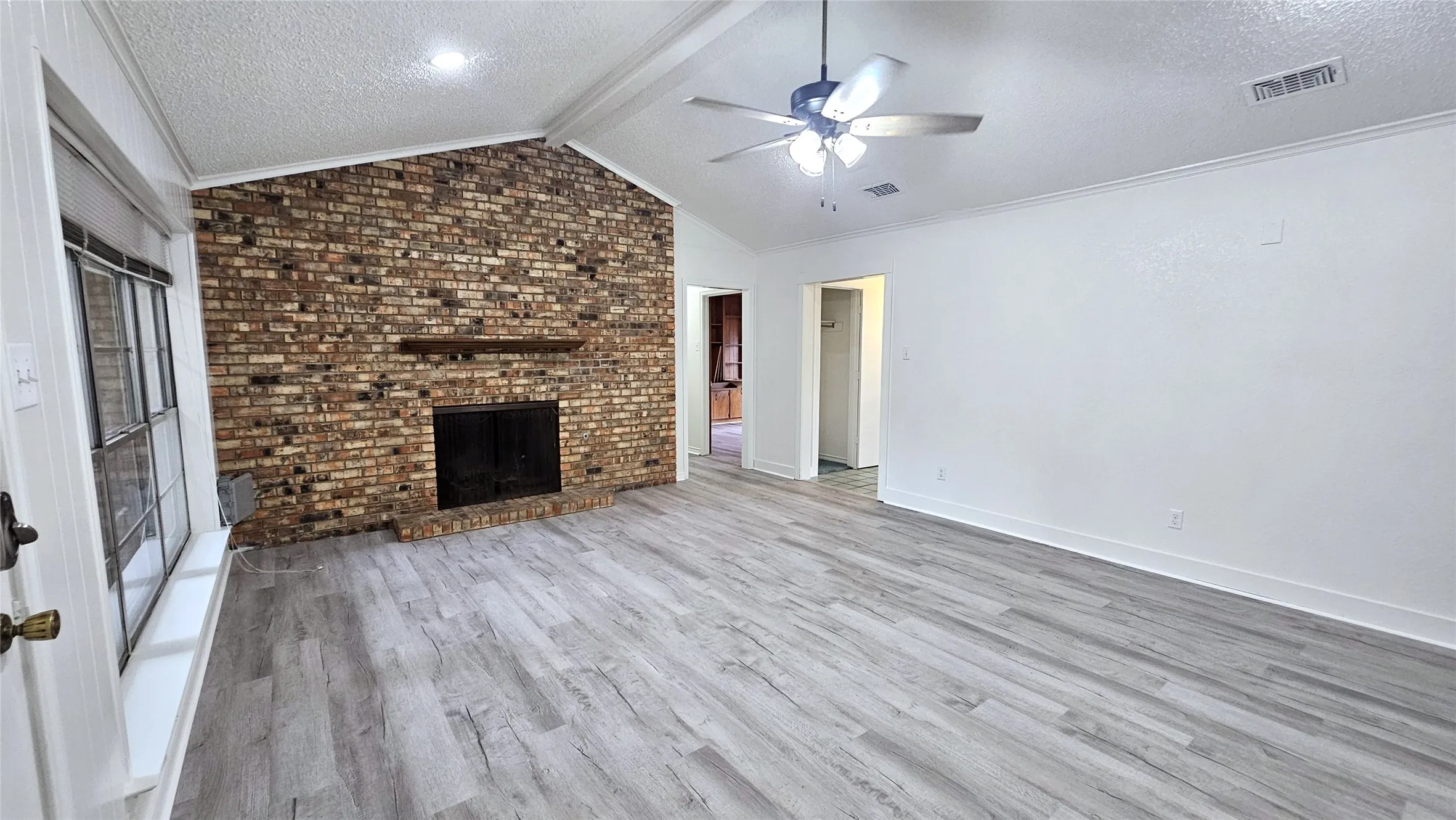 Living room featuring a ceiling fan, a full wall brick fireplace,  gray Luxury vinyl plank floors, Full wall bookshelf, and ornamental molding