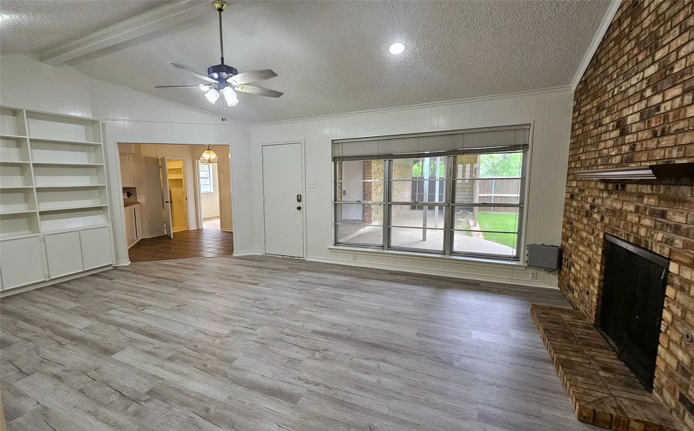 Living room featuring a ceiling fan, a full wall brick fireplace,  gray Luxury vinyl plank floors, Full wall bookshelf, and 3 large windows overlooking the back yard.