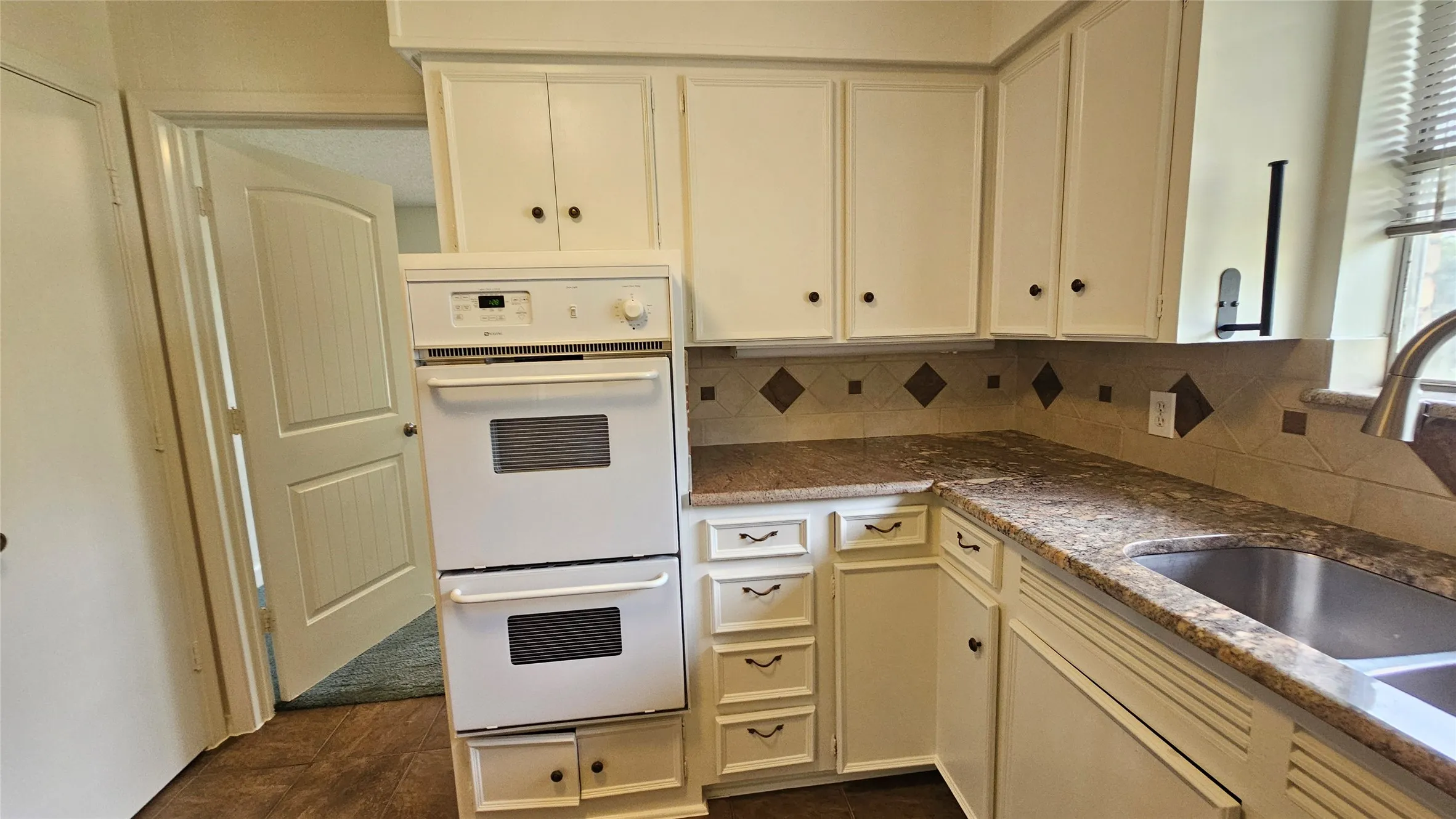 Kitchen featuring double oven, a sink, backsplash, and white cabinetry