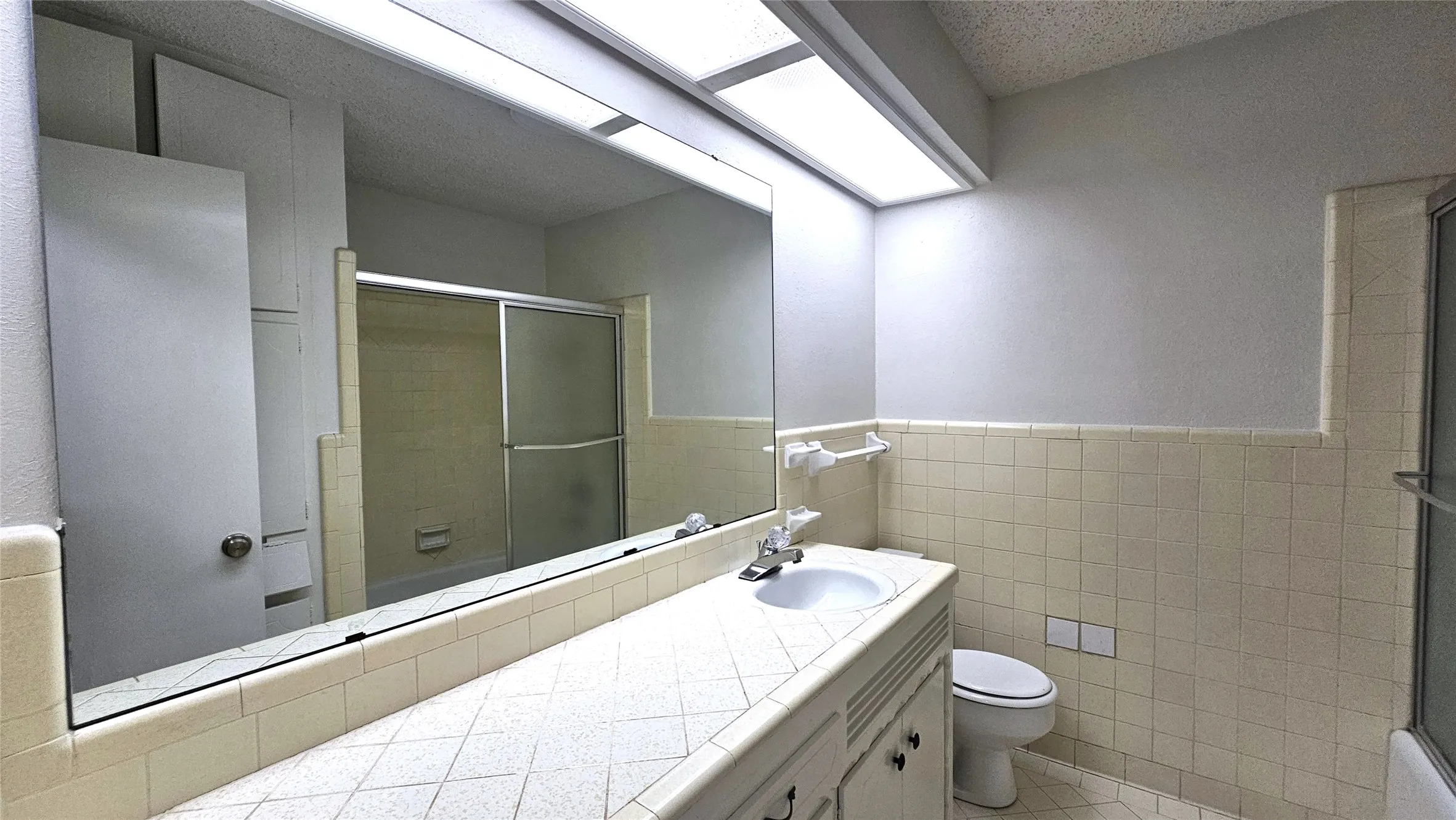 Full bath featuring a shower with door, toilet, a wainscoted wall, tile walls, and tile patterned flooring