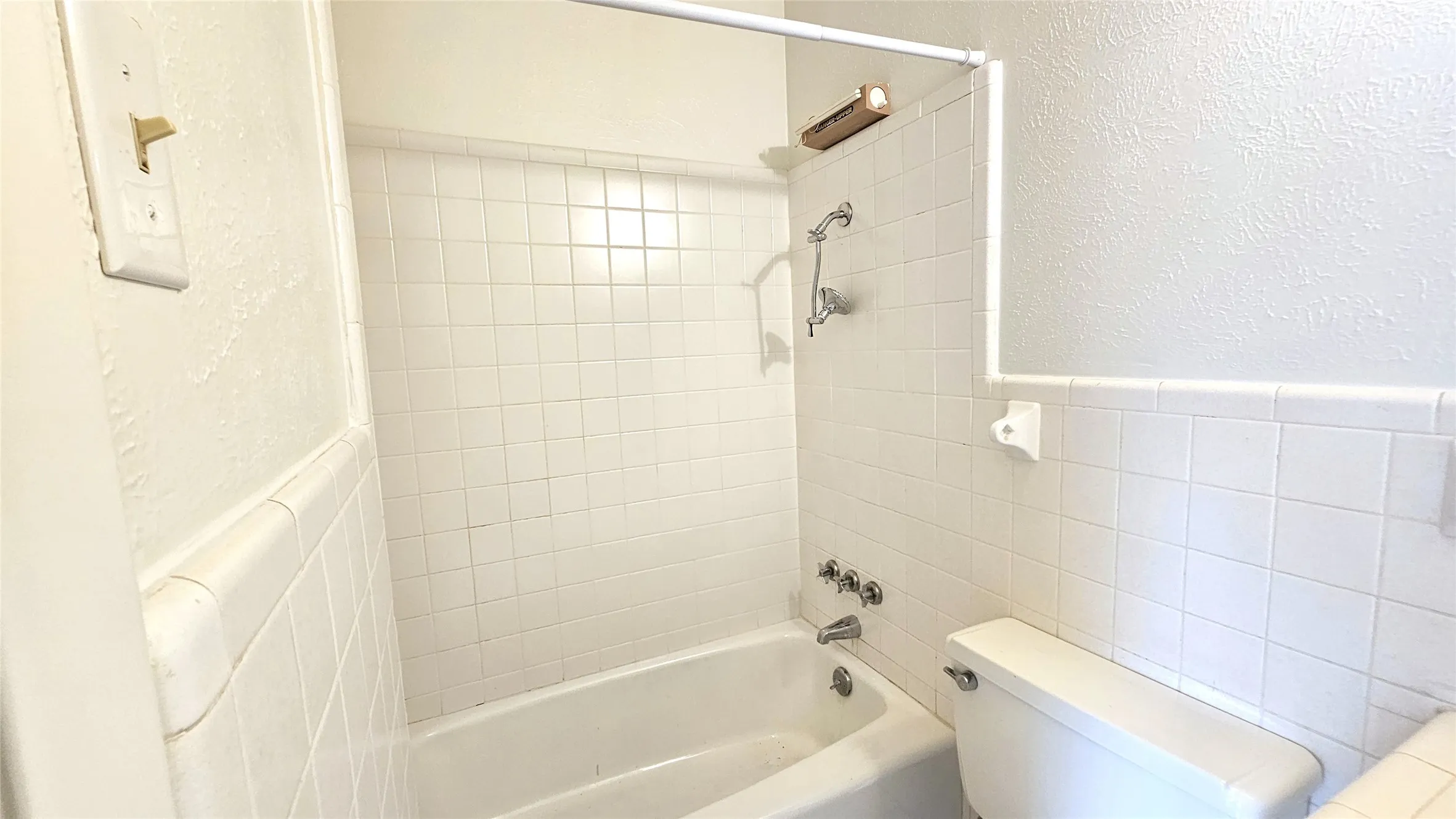 Ensuite Full bath of bedroom 4 featuring tile walls, toilet, bathing tub / shower combination, wainscoting, and a textured wall