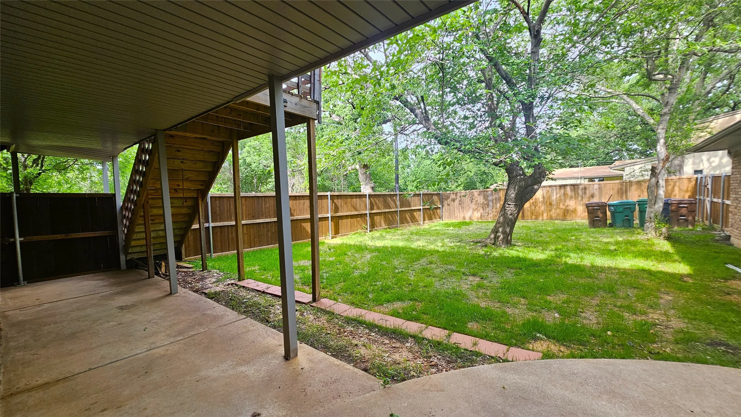 View of yard featuring a long covered patio area. Yard stays shaded in the afternoon shielded by the big trees and the home.