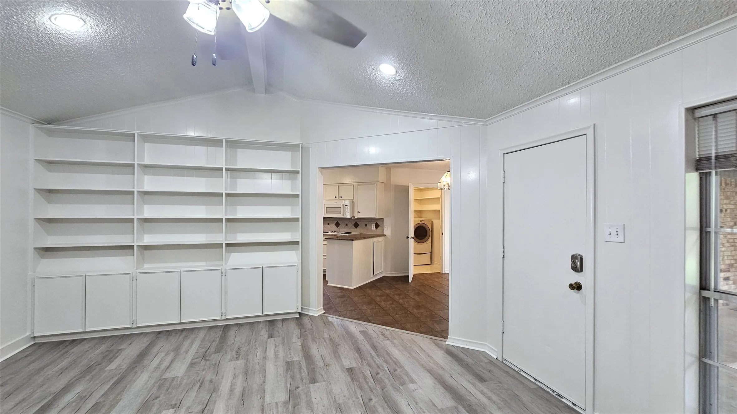 Living room featuring a ceiling fan, a full wall brick fireplace,  gray Luxury vinyl plank floors, Full wall bookshelf, and ornamental molding