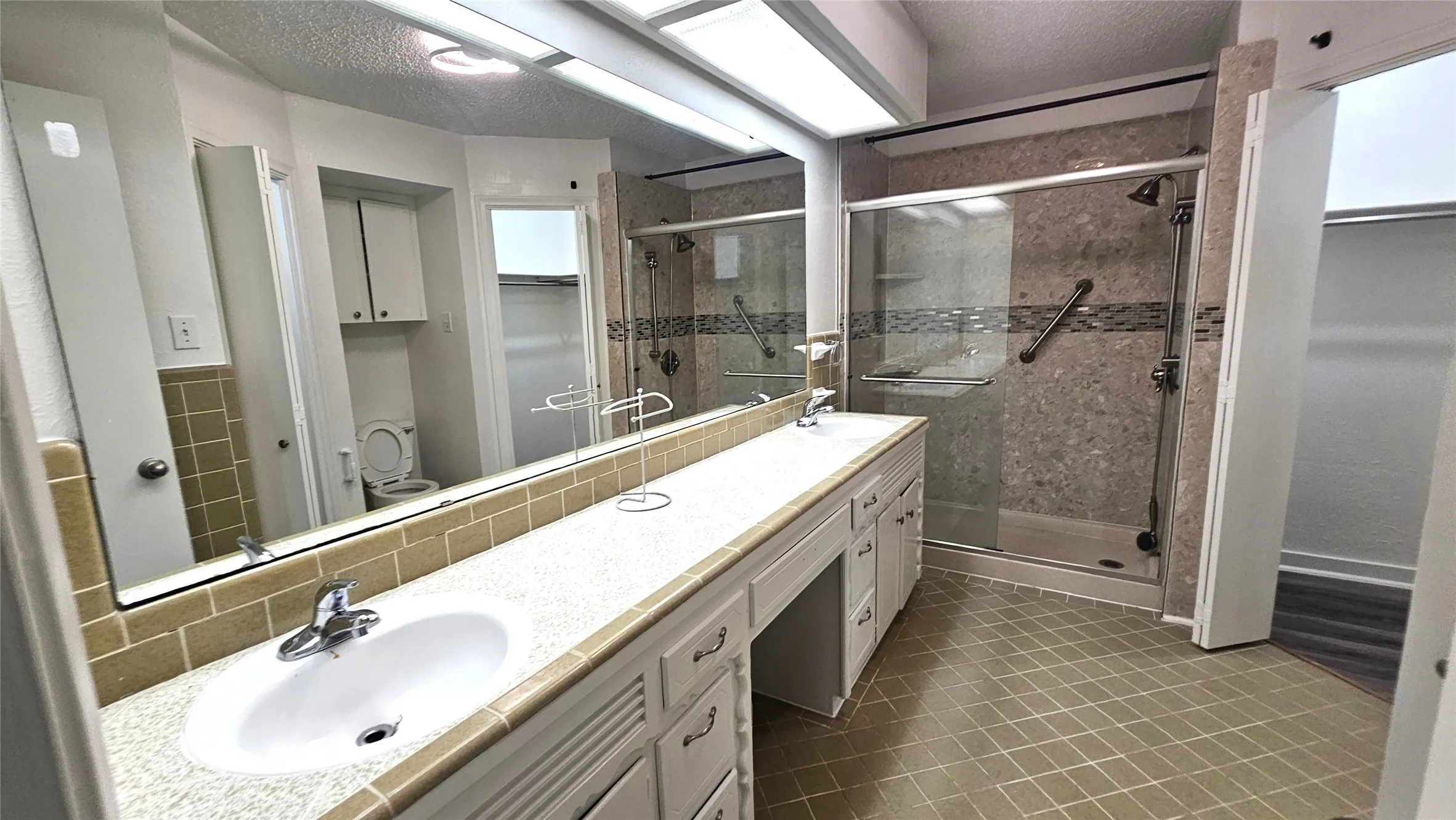 Primary Full bathroom featuring Long tile countertop with vanity make up area, a modern shower stall, tile floors, and a textured ceiling