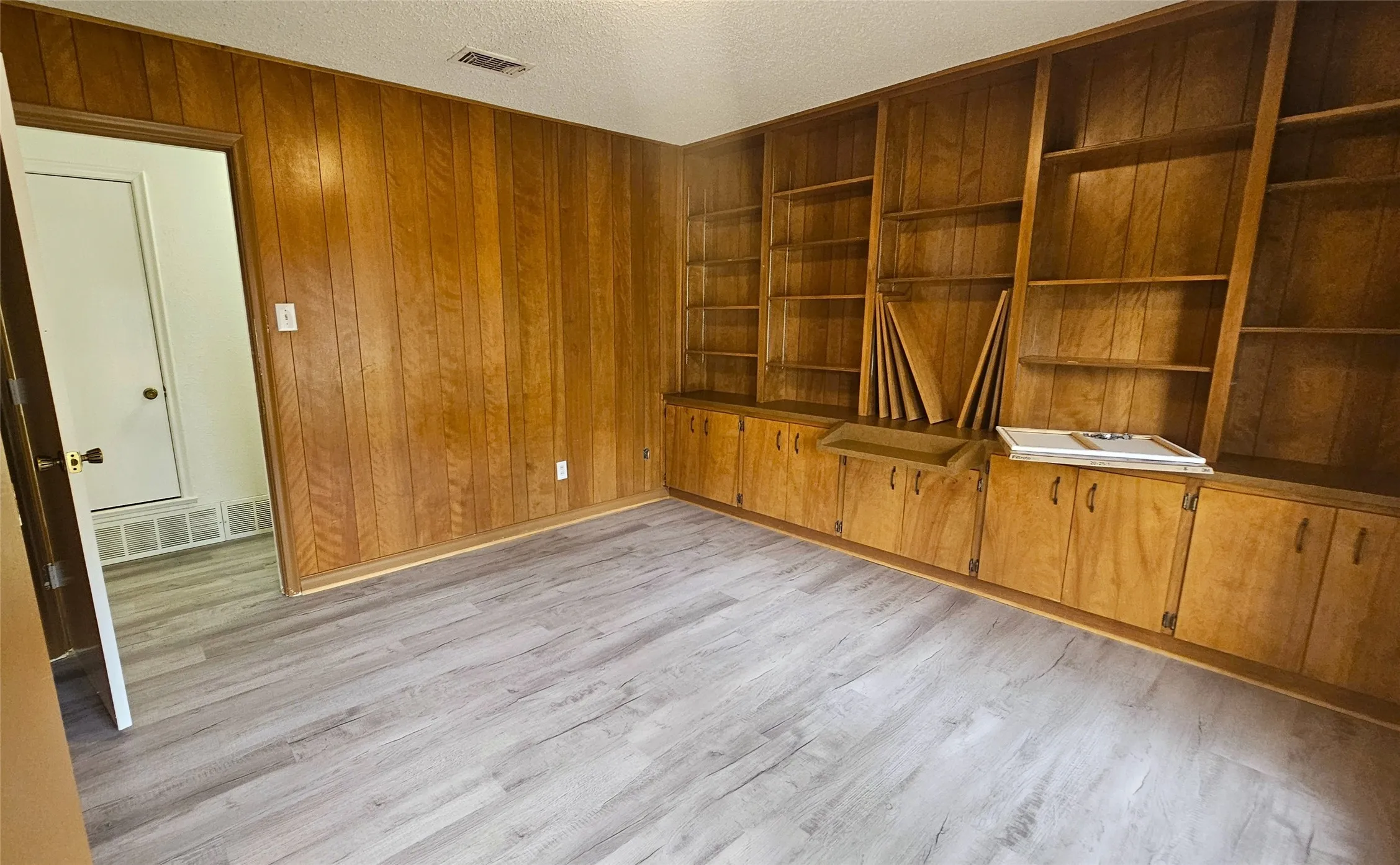 Bedroom 5 with gray luxury vinyl plank floors, windows facing front yard, wall of bookshelves with stained wood and storage. Would be great study or teaching room as well!