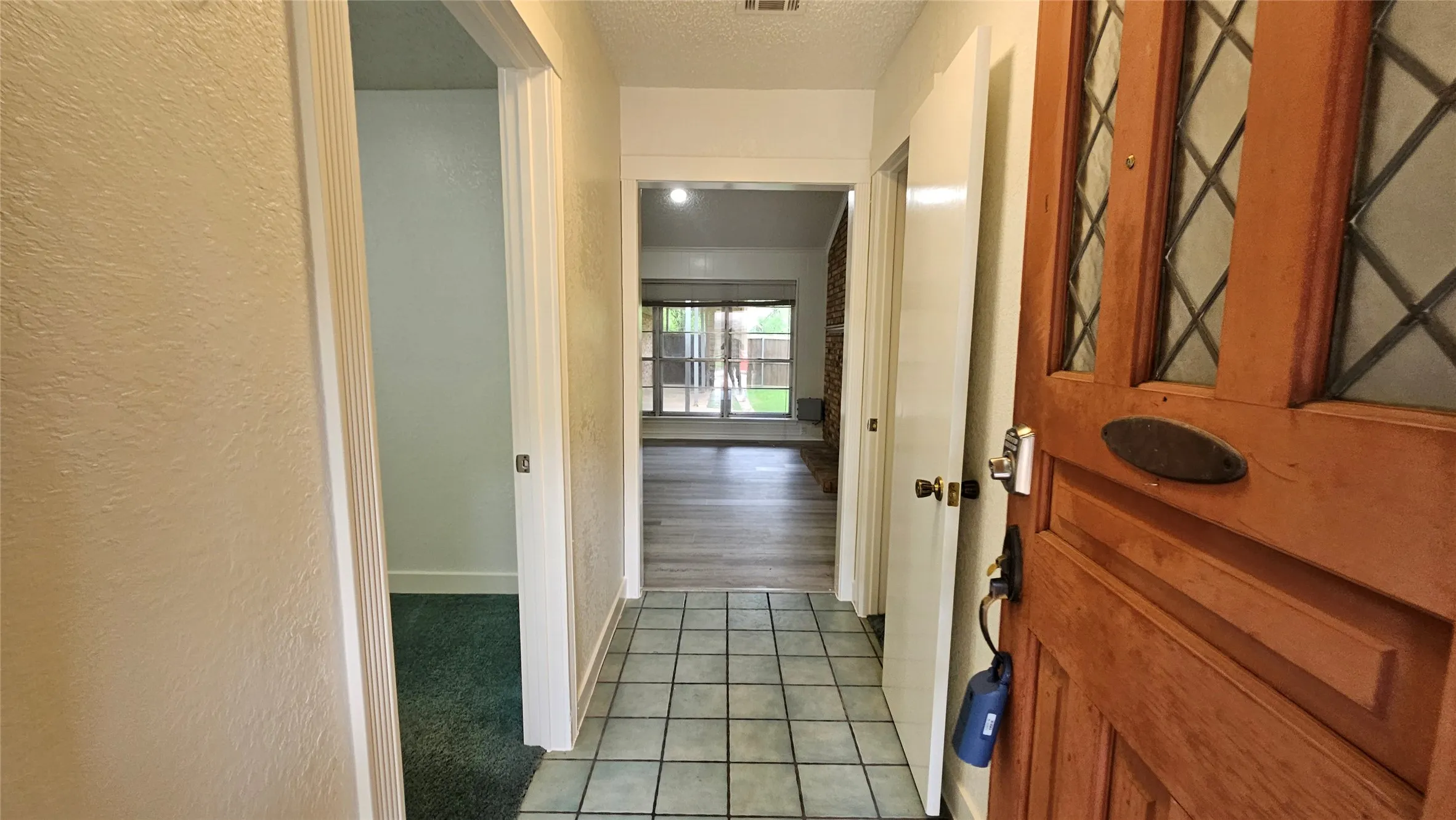Hall with light tile patterned floors, a textured wall, baseboards, and a textured ceiling
