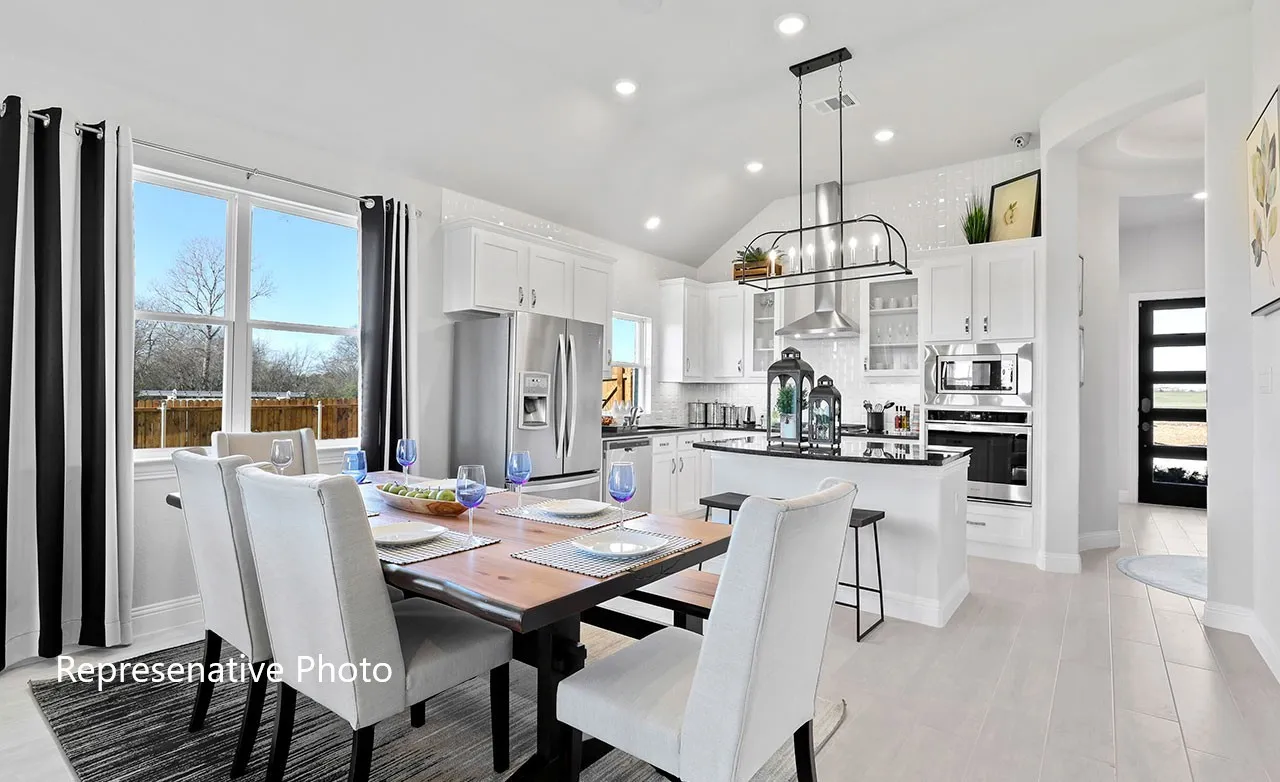 Open-concept living space featuring a spacious kitchen with white cabinetry and stainless steel appliances, a center island with a black countertop, and a dining area with wood-finish flooring