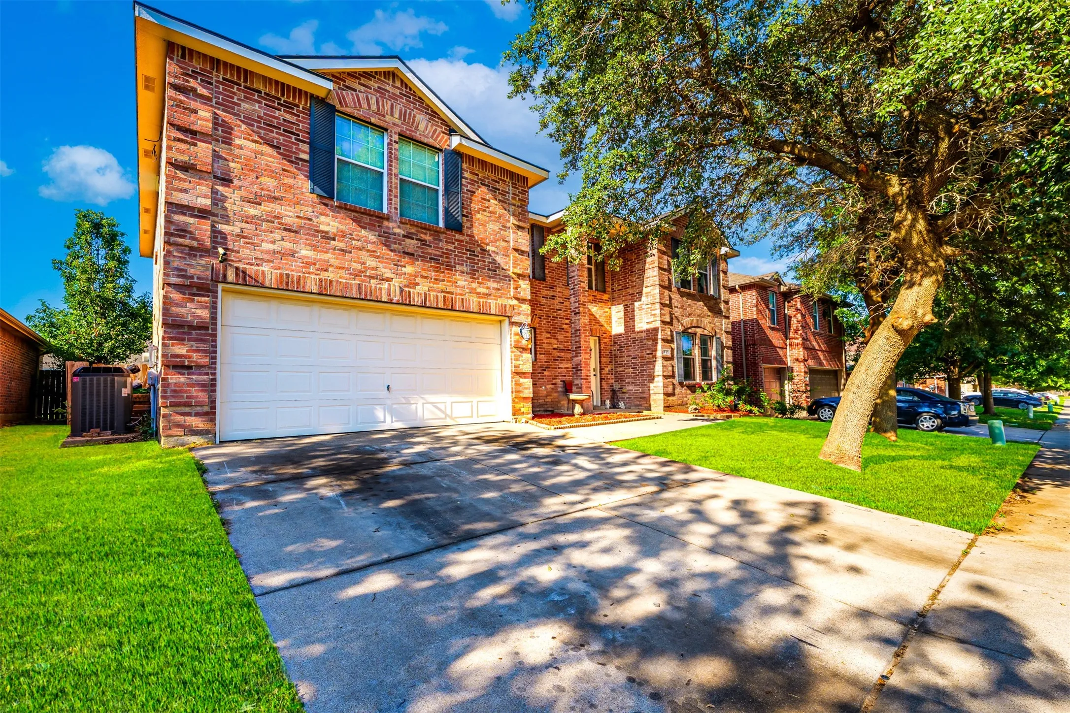 Brick facade residence featuring a two-car garage, concrete driveway, and established front yard landscaping