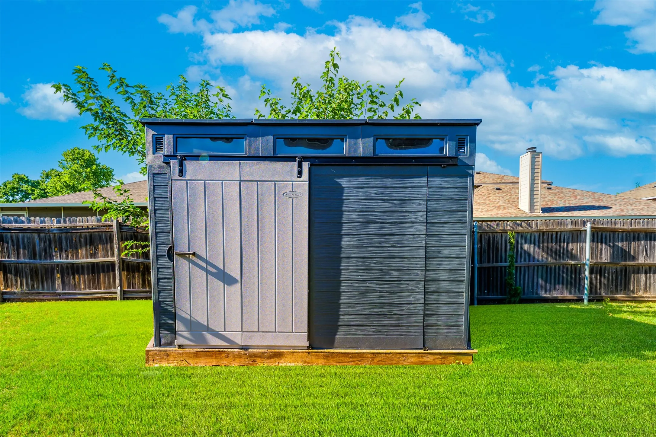 Contemporary storage shed featuring a dual-tone exterior, clerestory windows, a sliding door, and a durable base, situated on a vibrant green lawn