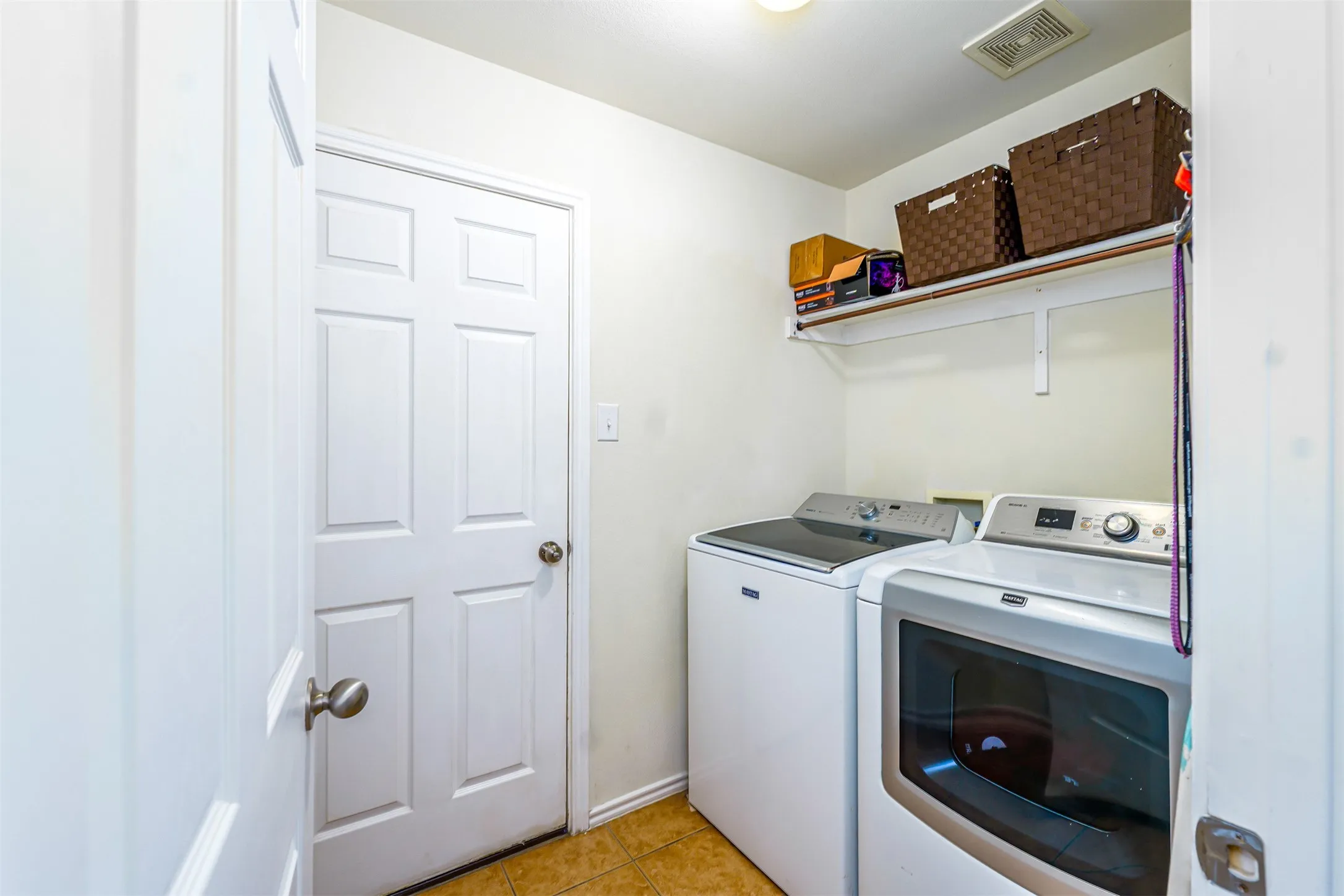 Dedicated laundry area featuring a white six-panel door, neutral wall paint, and overhead shelving for storage