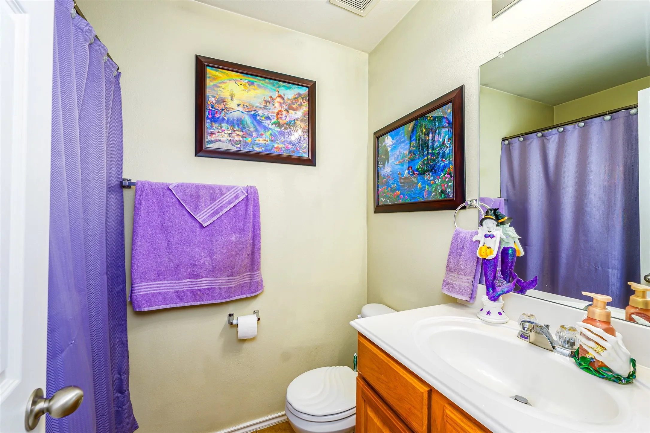 Bathroom featuring a wood-finish vanity with an integrated white sink, a wall-mounted mirror, and a toilet