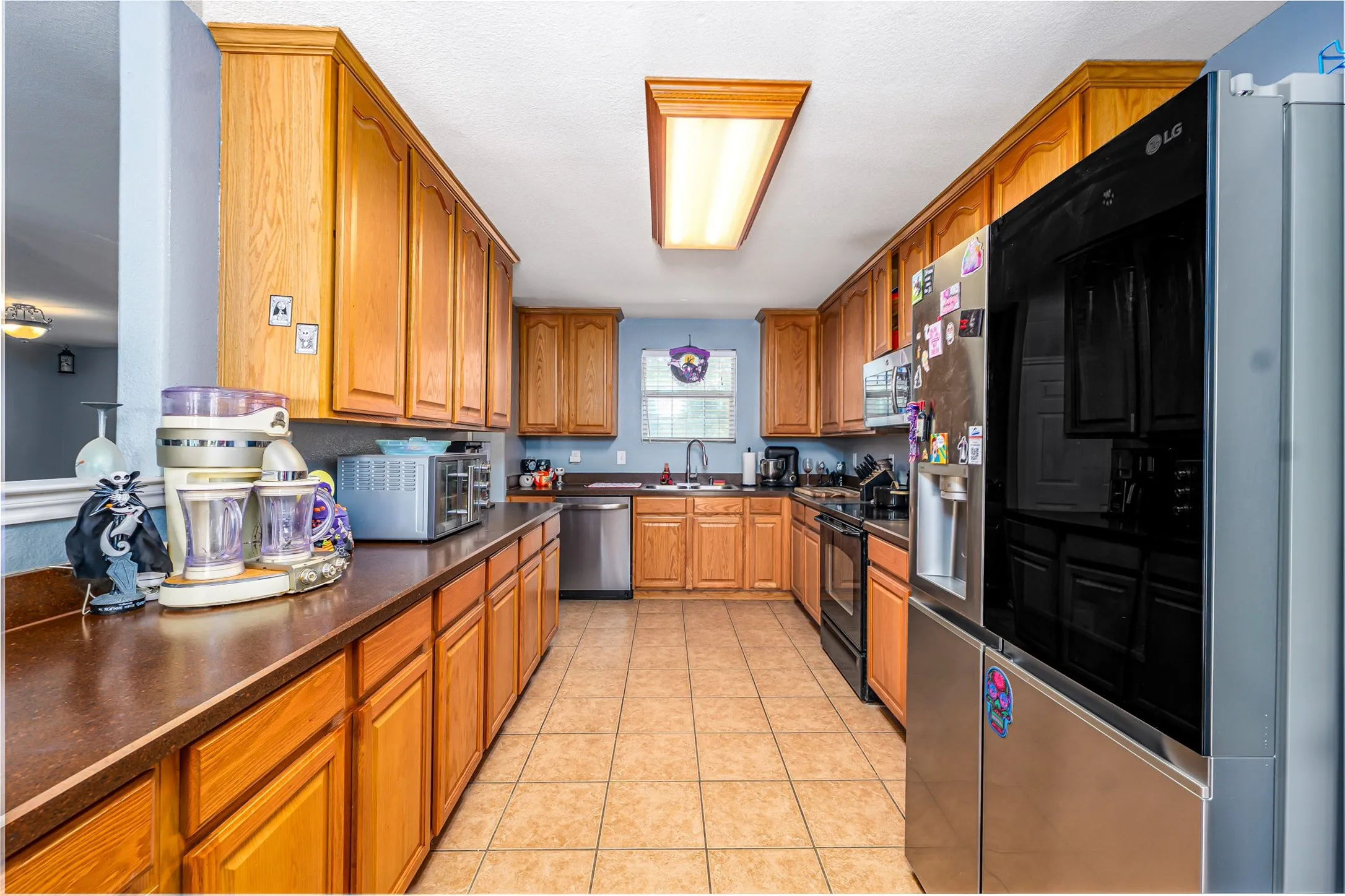Galley-style kitchen featuring wood cabinetry, brown countertops, and tile flooring