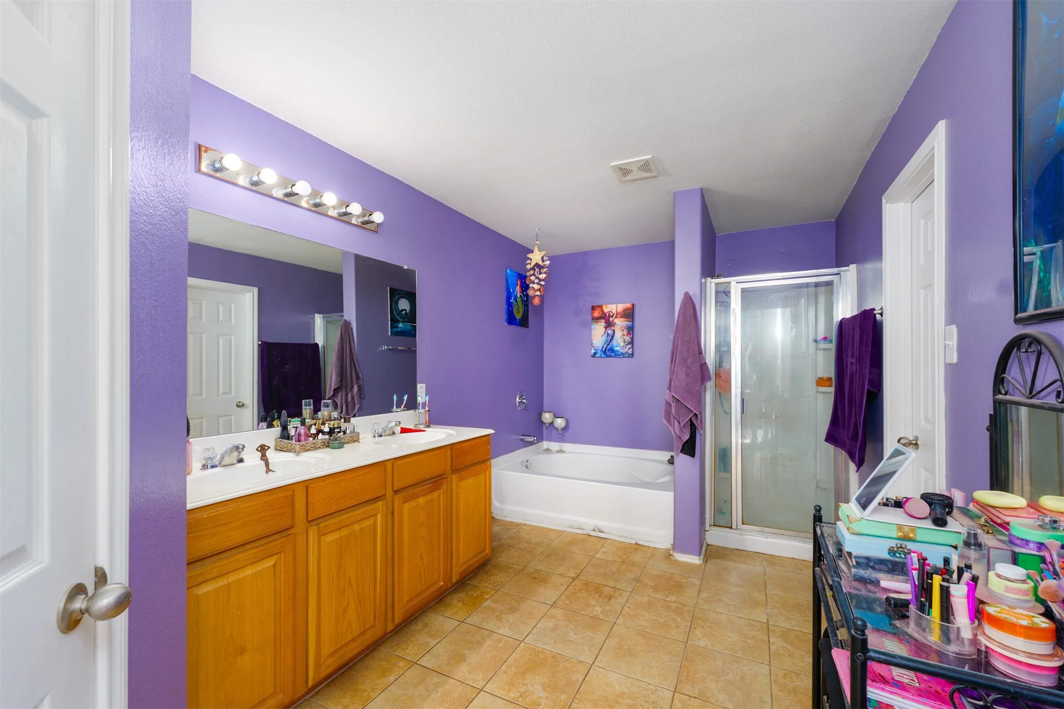 Bathroom featuring a double vanity with light wood cabinetry, a large wall-mounted mirror, and a multi-bulb vanity light fixture