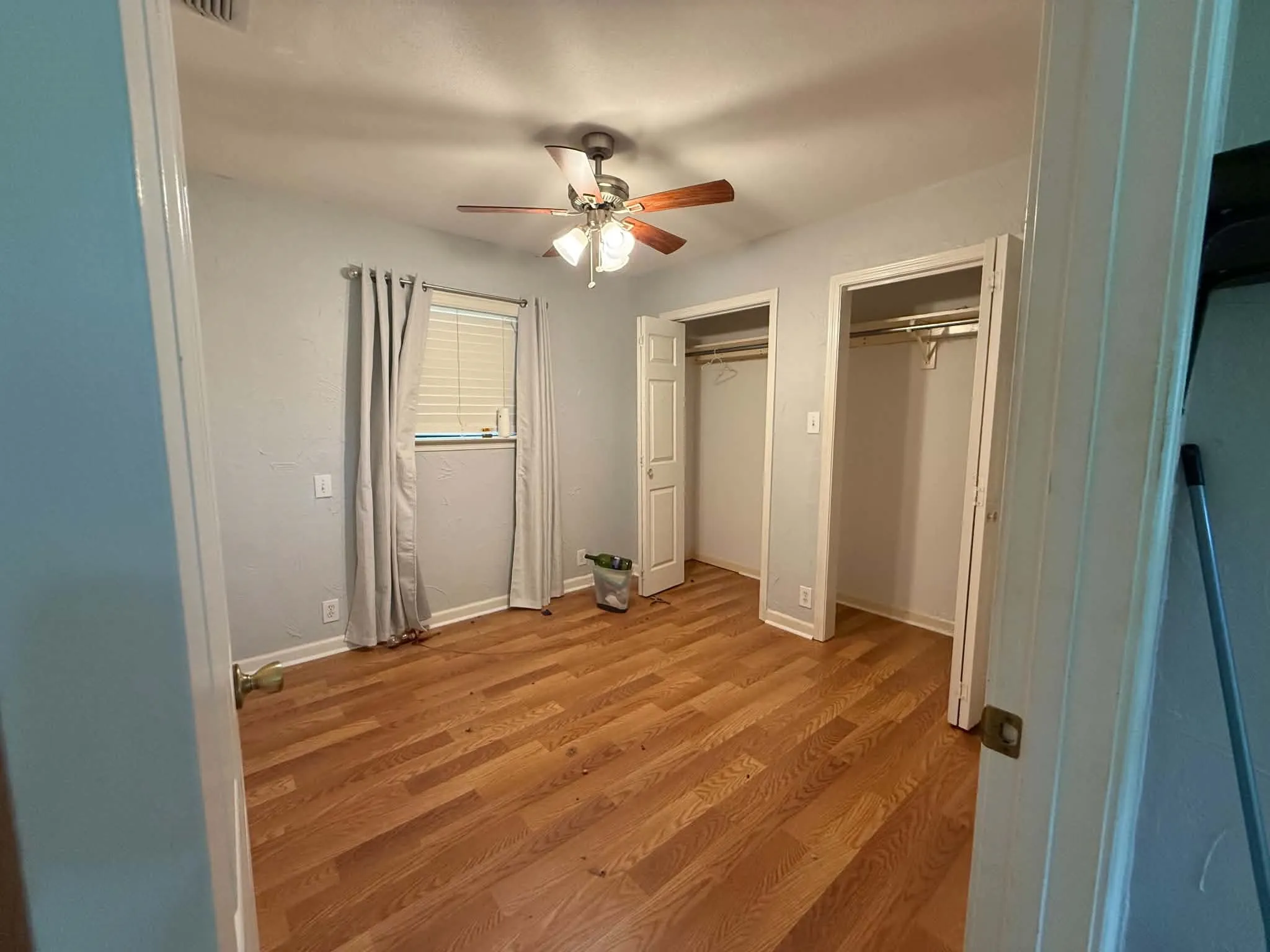 Spacious room featuring wood-finish flooring, a window with horizontal blinds, and a ceiling fan