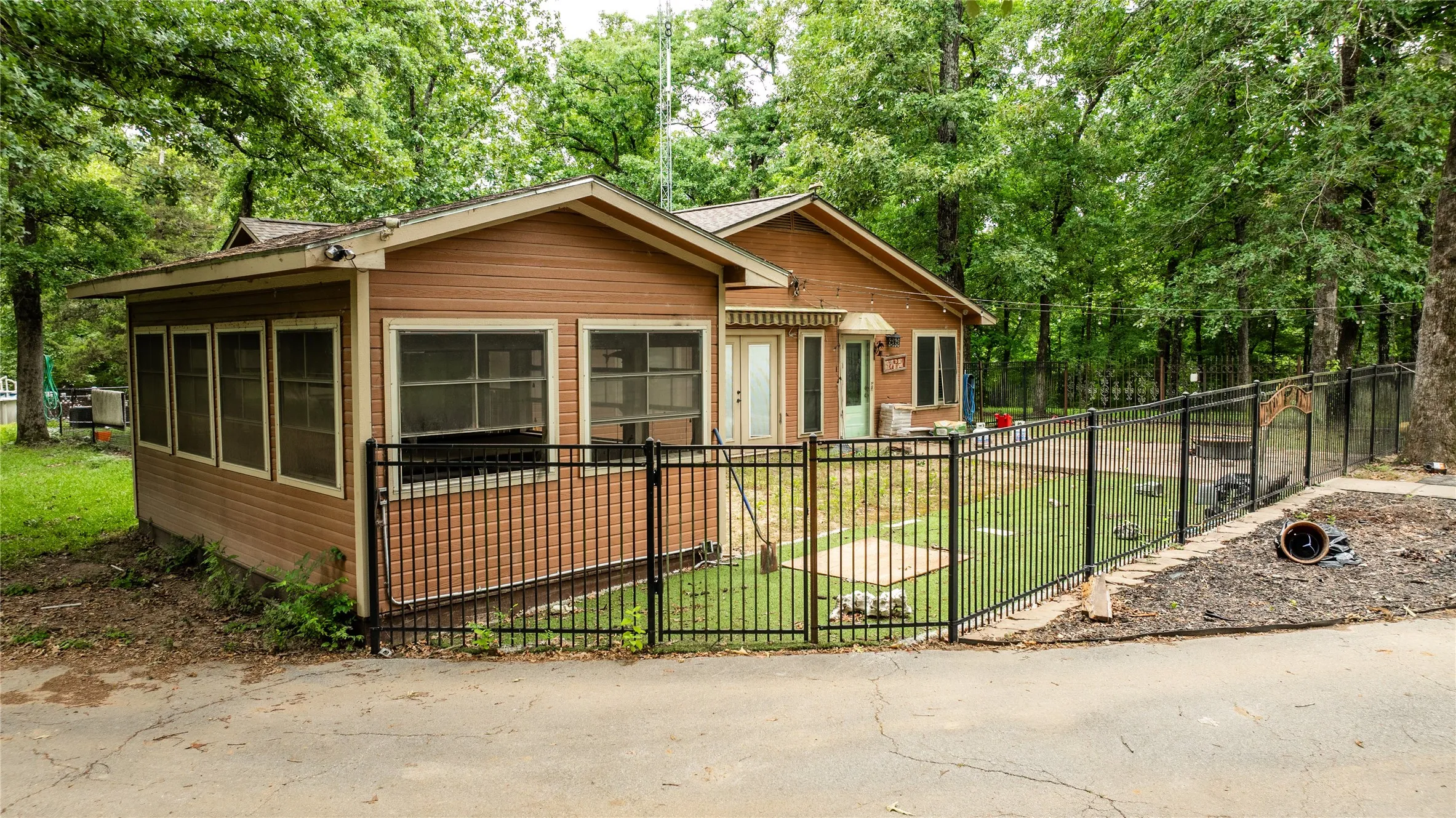 Single-story dwelling with light brown siding, a screened-in porch, and a fenced yard featuring artificial turf