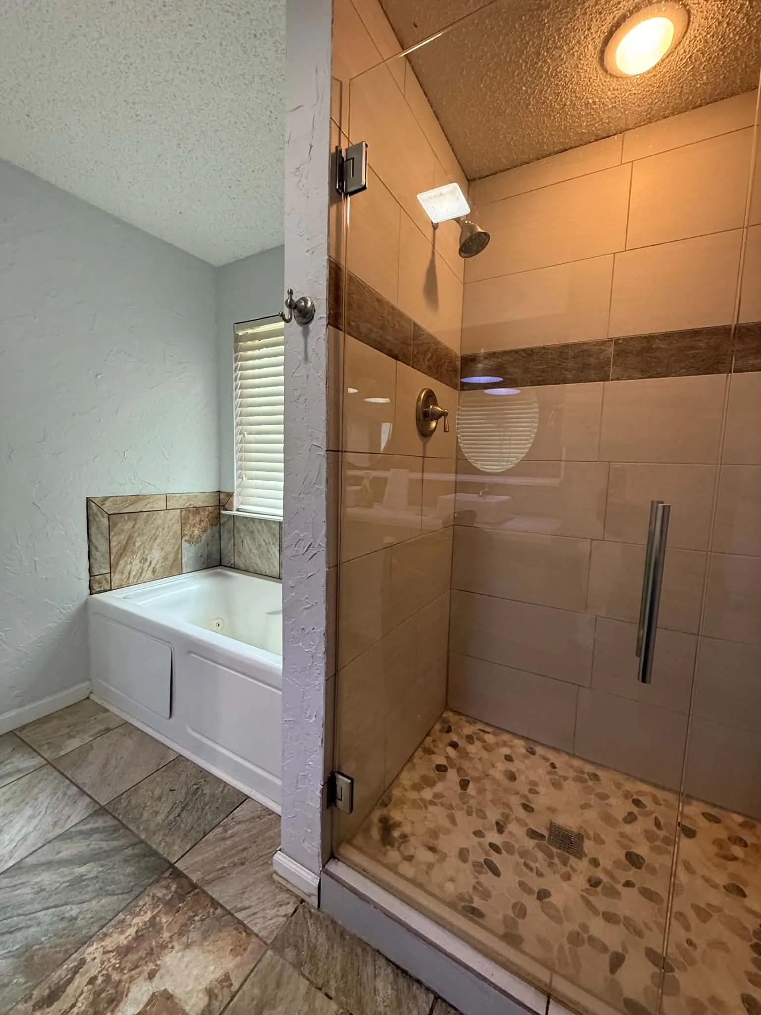 Glass-enclosed shower with pebble-style floor and overhead lighting