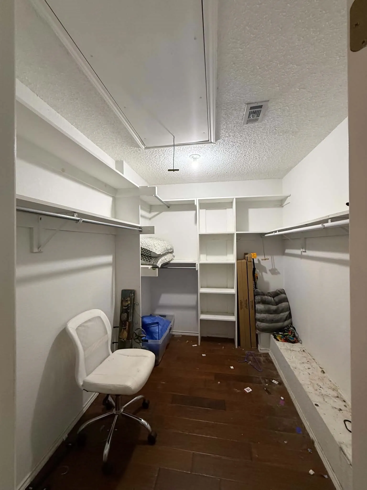 Built-in shelving and hanging rods in a white-painted interior, featuring wood-finish flooring and an overhead light fixture