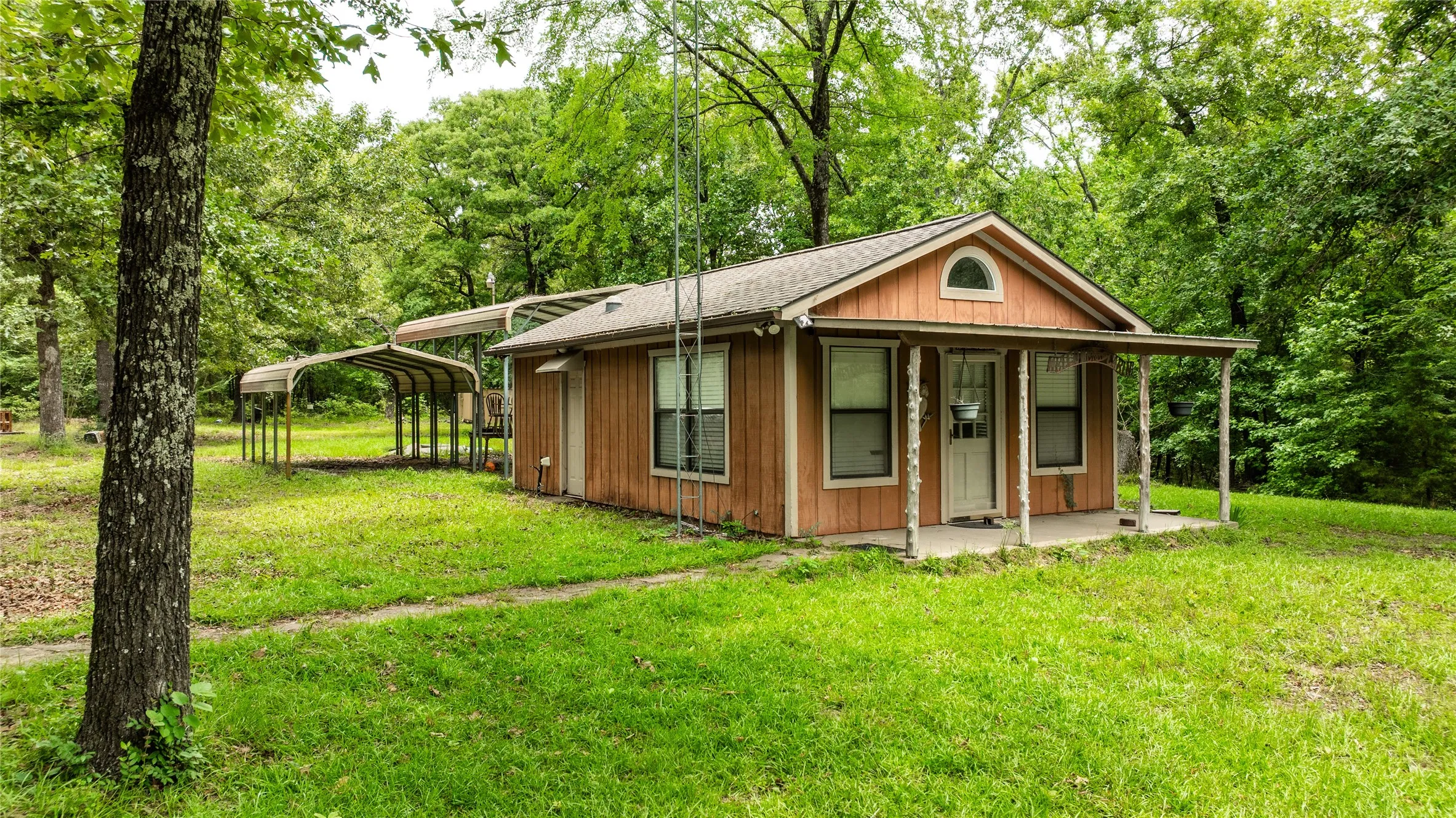 Wood-sided structure with an arched gable window, covered front porch, and multiple detached carports